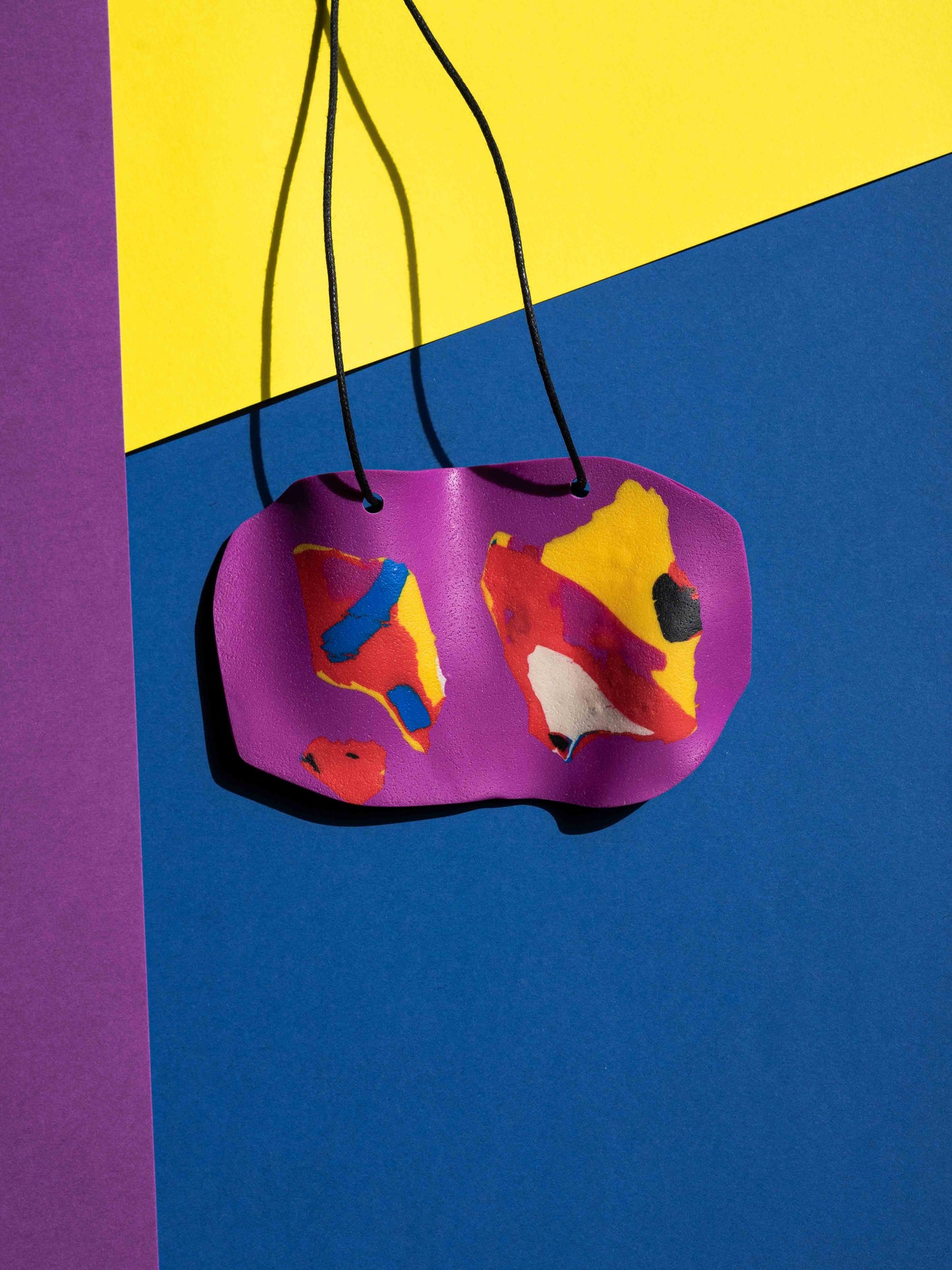 Front view of a salvaje pendant in magenta, yellow, red, blue and purple colours with strong lighting on a colourful background
