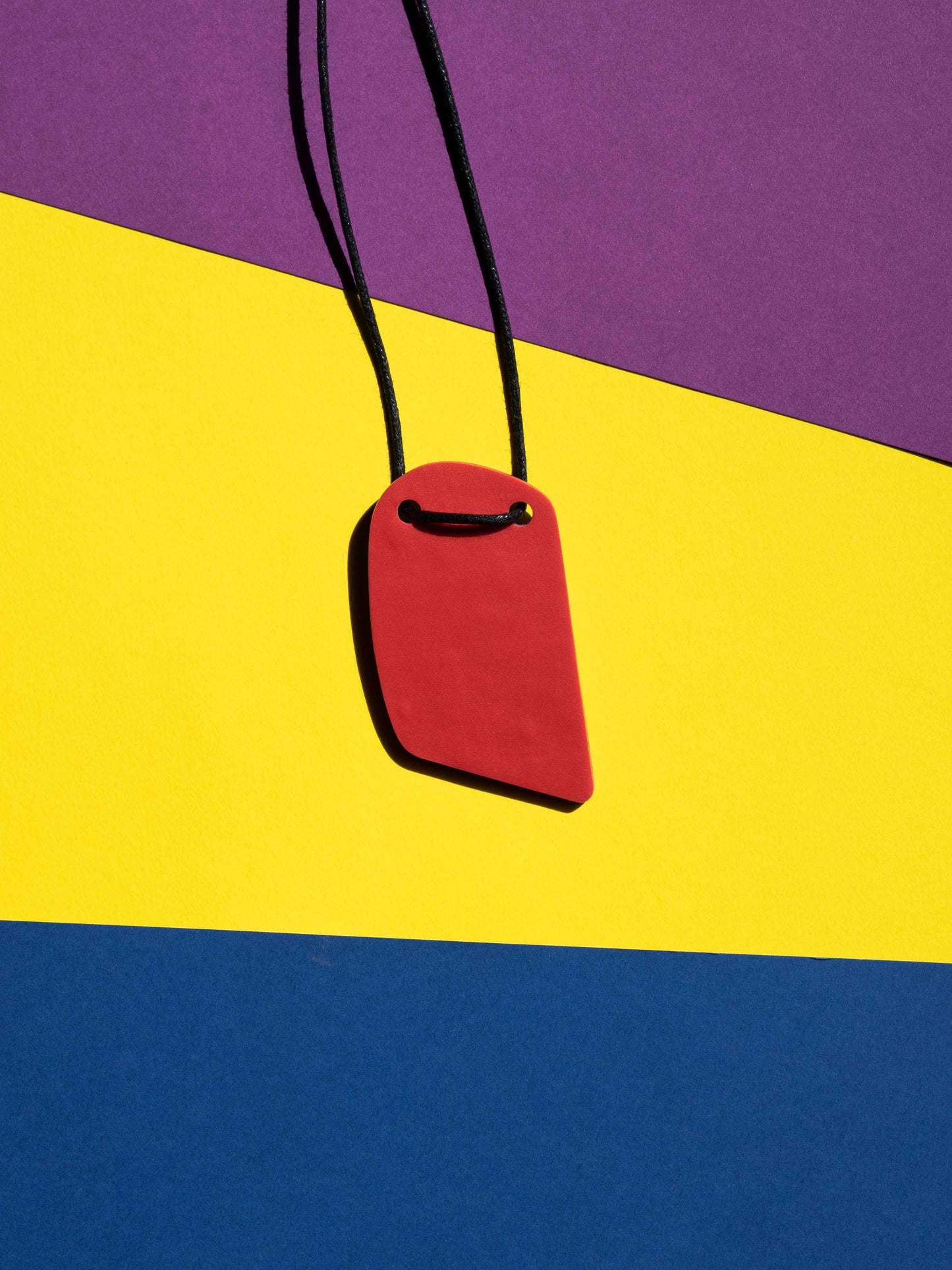 Back red view of a salvaje pendant in purple, magenta, yellow, blue, black and red colours with strong lighting on a colourful background