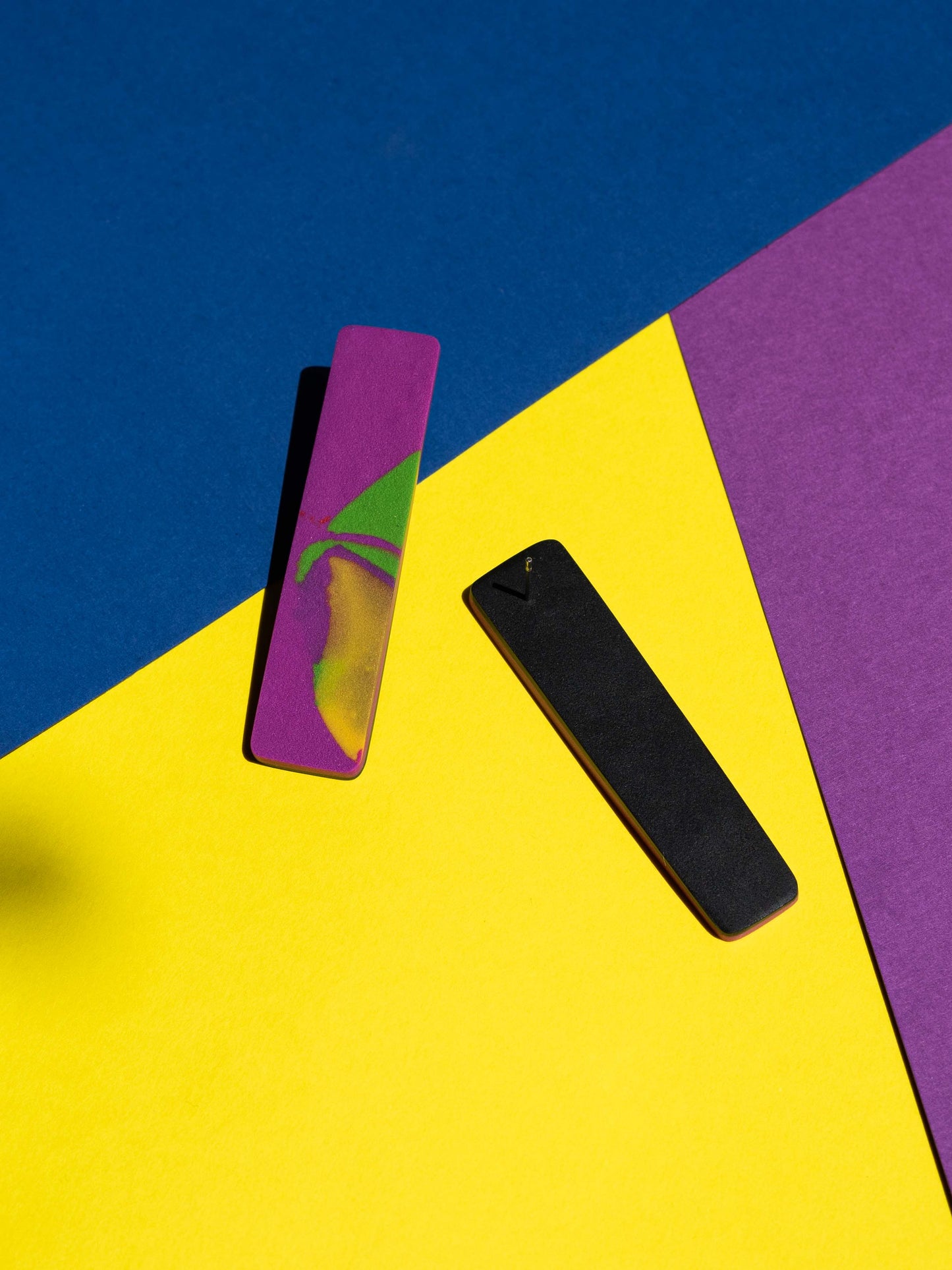 Front and back views of two original Salvaje studs, handmade in polymer clay, photographed on a colourful background under direct sunlight.