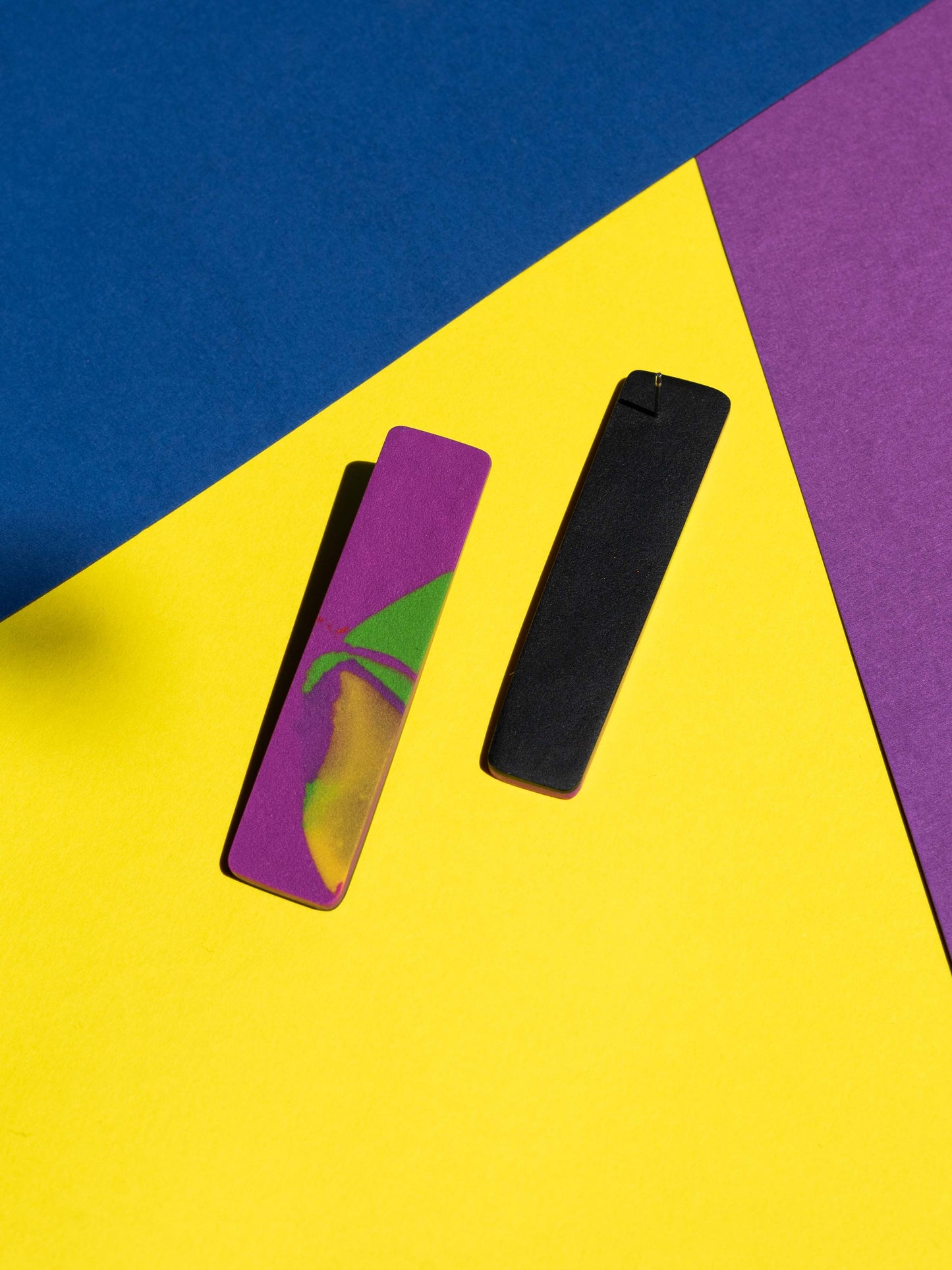 Front and back views of two original Salvaje studs, handmade in polymer clay, photographed on a colourful background under direct sunlight.
