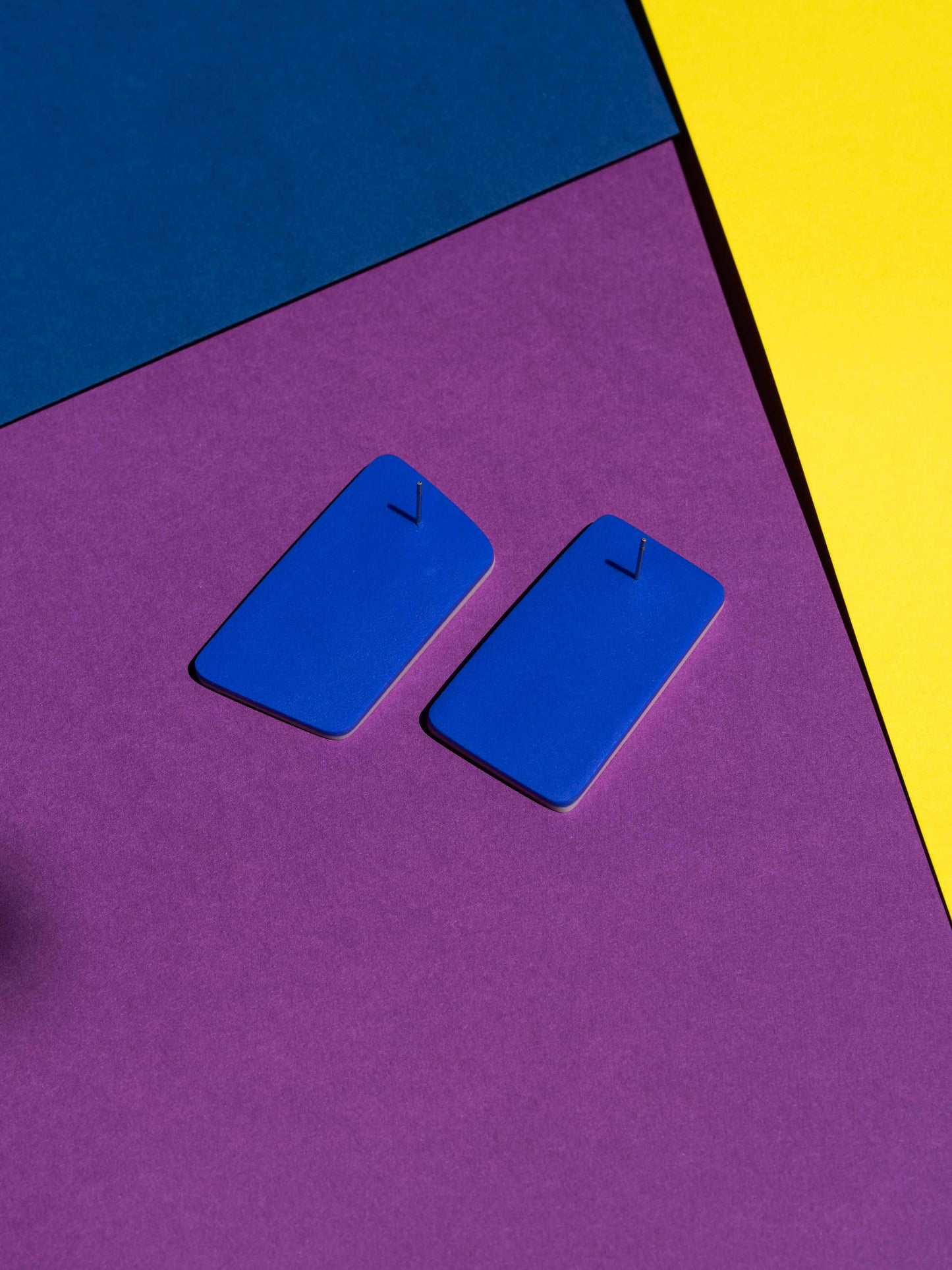Back view of two original Salvaje studs, handmade in polymer clay, photographed on a colourful background under direct sunlight.