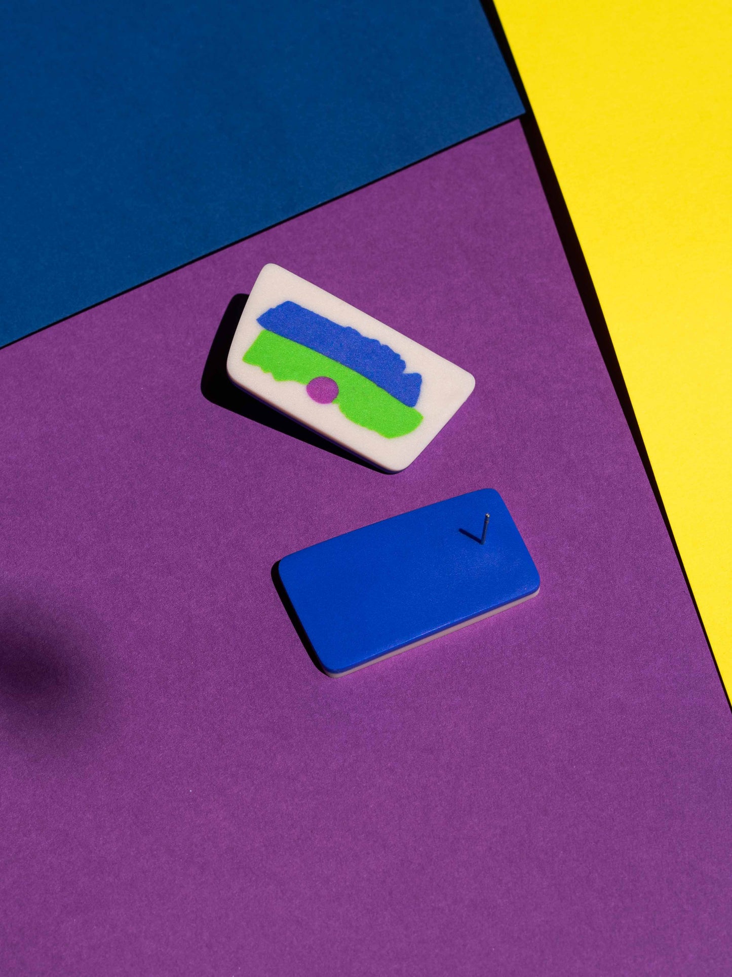 Front and back views of two original Salvaje studs, handmade in polymer clay, photographed on a colourful background under direct sunlight.