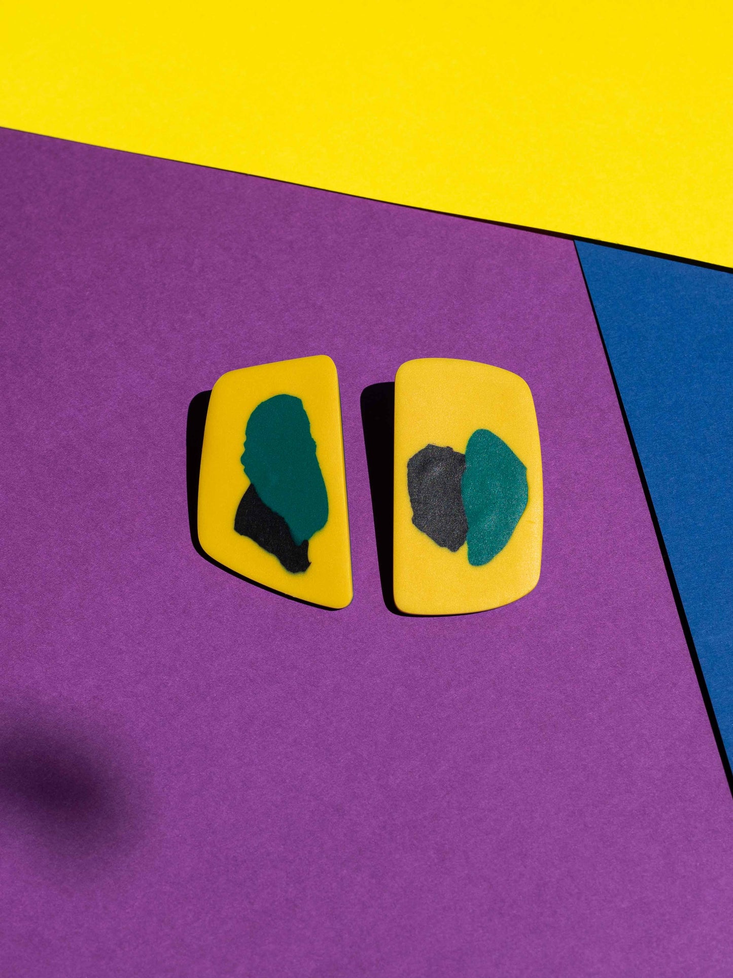 Front view of two original Salvaje studs, handmade in polymer clay, photographed on a colourful background under direct sunlight.