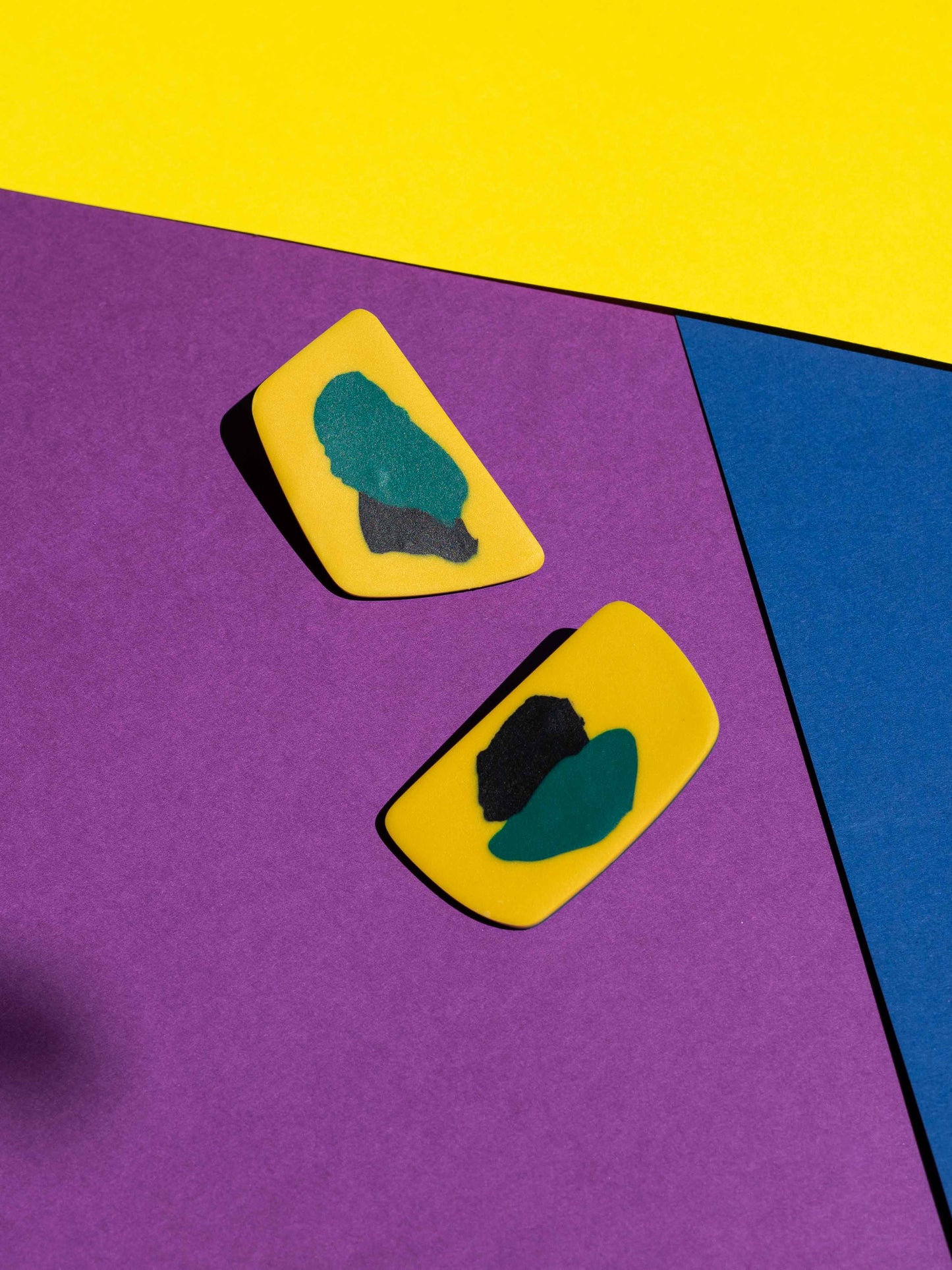 Front view of two original Salvaje studs, handmade in polymer clay, photographed on a colourful background under direct sunlight.