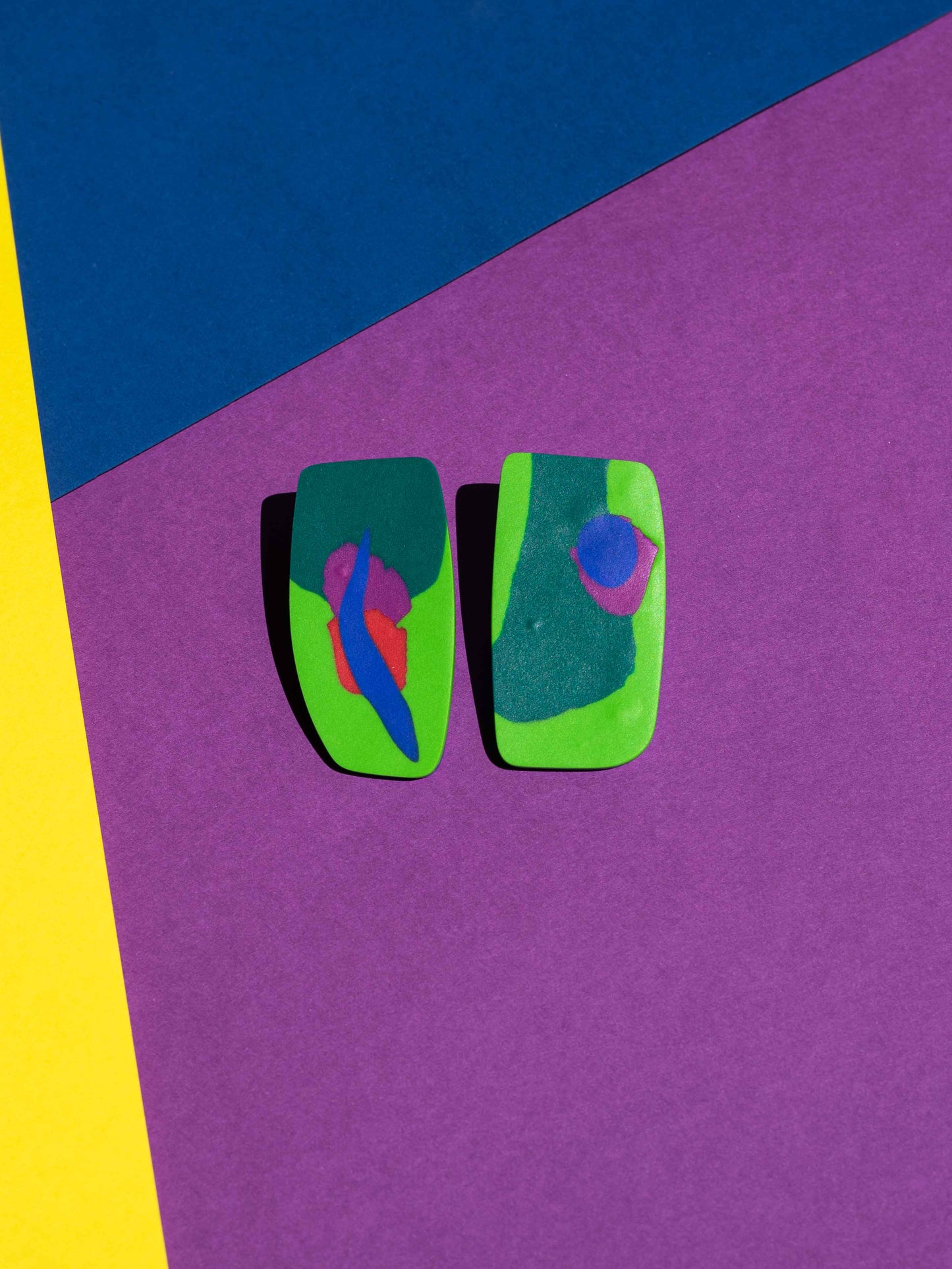 Front view of two original Salvaje studs, handmade in polymer clay, photographed on a colourful background under direct sunlight.