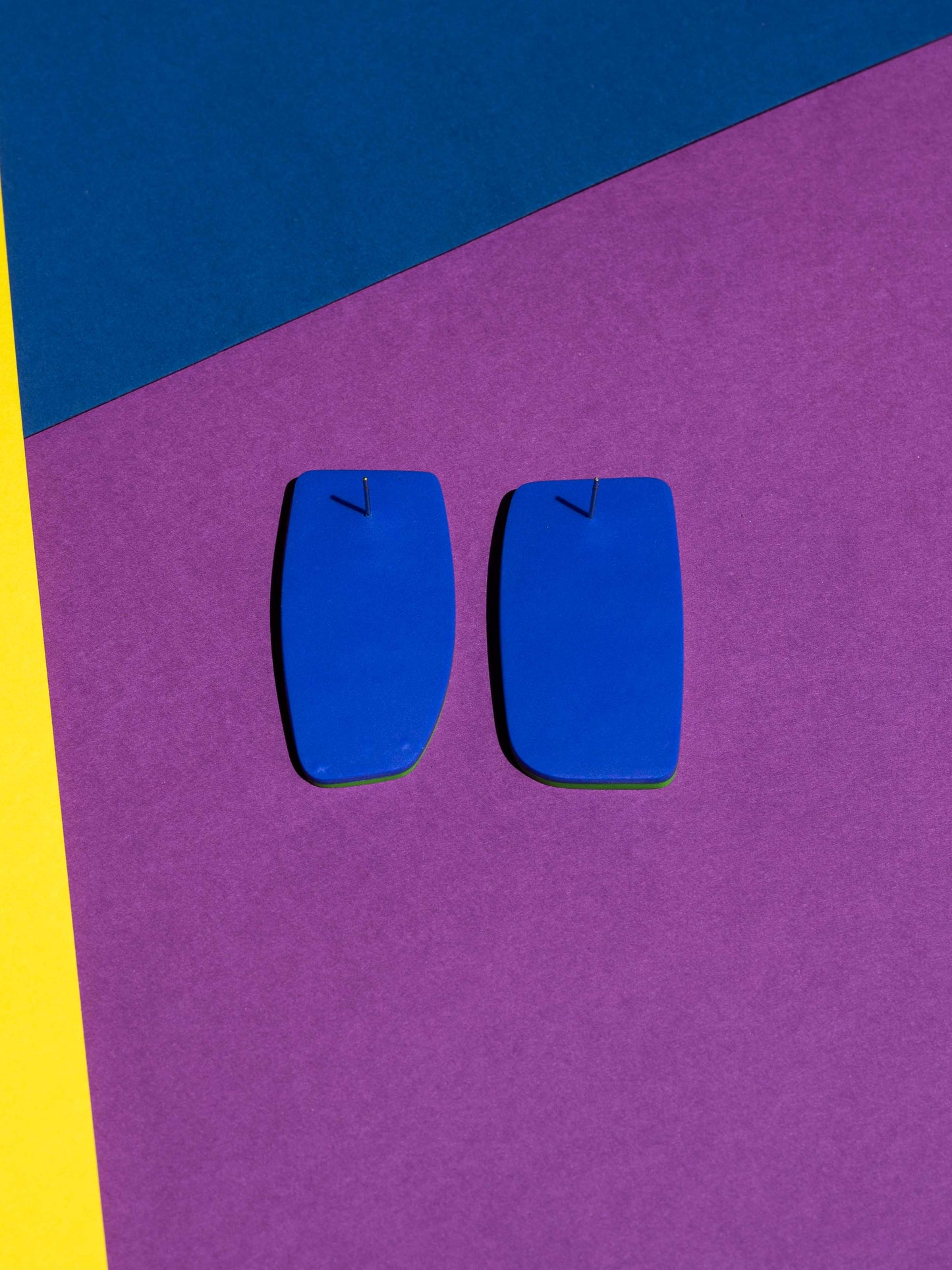 Back view of two original Salvaje studs, handmade in polymer clay, photographed on a colourful background under direct sunlight.