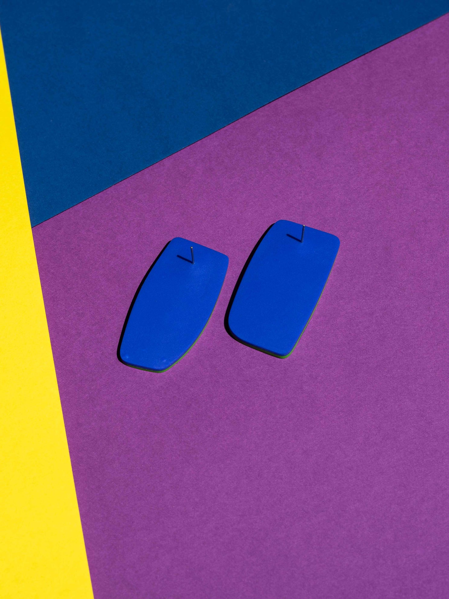 Back view of two original Salvaje studs, handmade in polymer clay, photographed on a colourful background under direct sunlight.