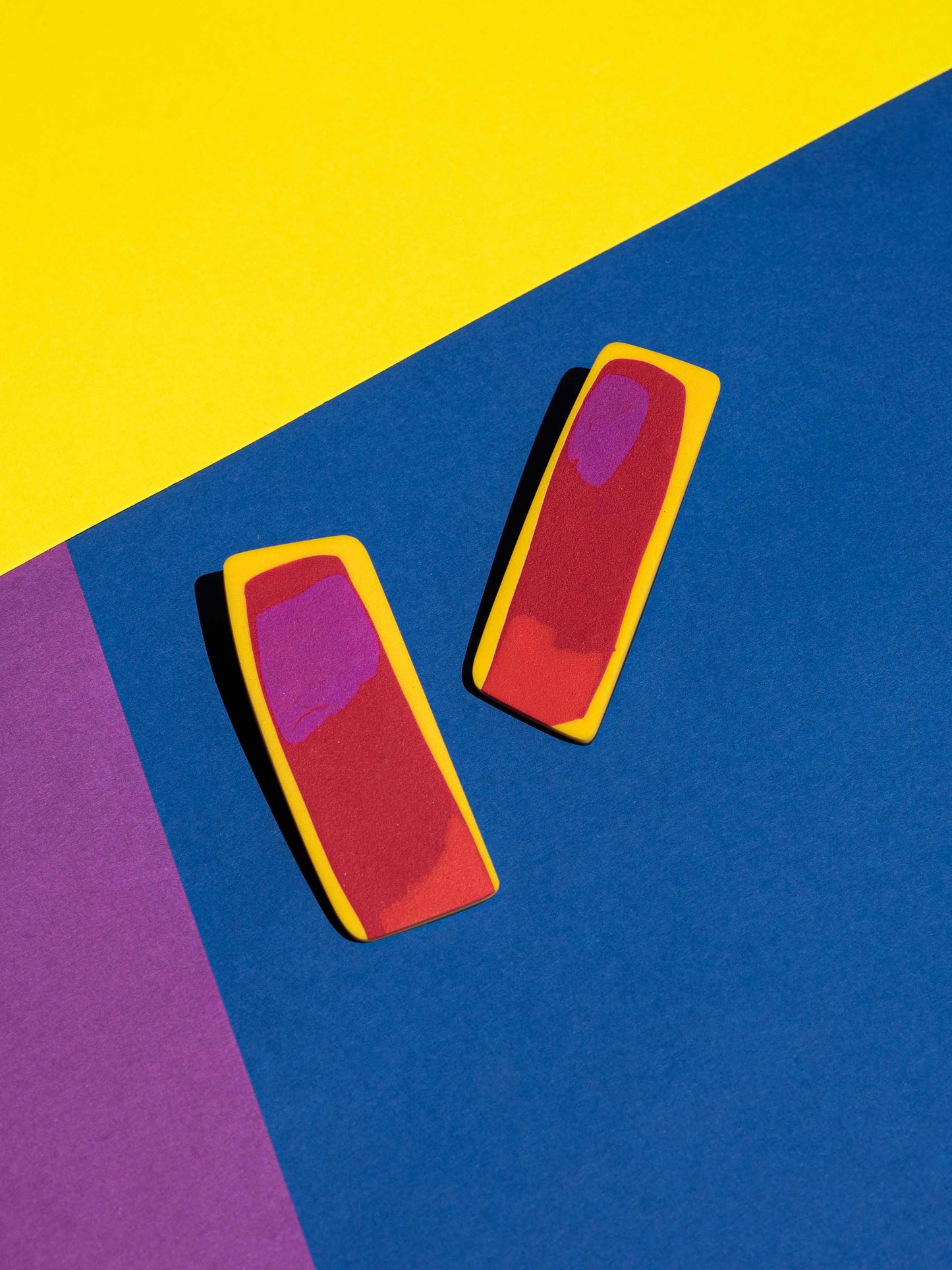 Front view of two original Salvaje studs, handmade in polymer clay, photographed on a colourful background under direct sunlight.