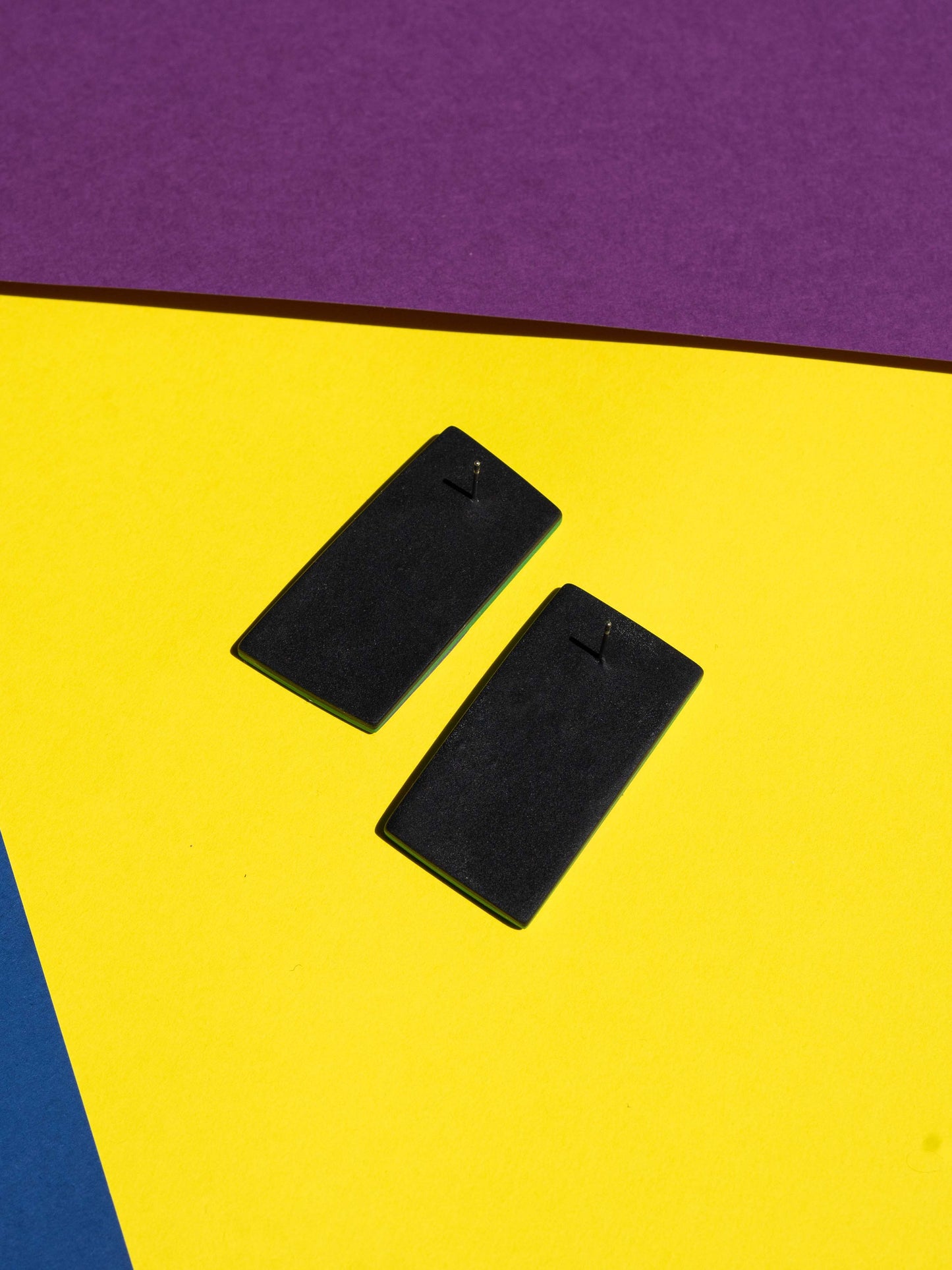 Back view of two original Salvaje studs, handmade in polymer clay, photographed on a colourful background under direct sunlight.