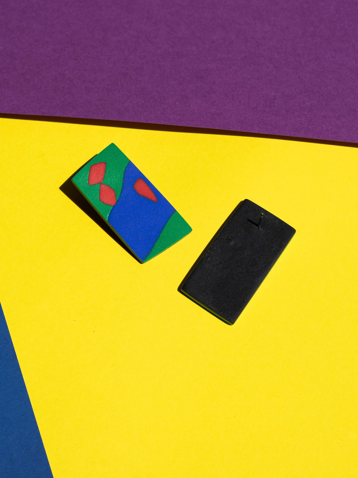 Front and back views of two original Salvaje studs, handmade in polymer clay, photographed on a colourful background under direct sunlight.