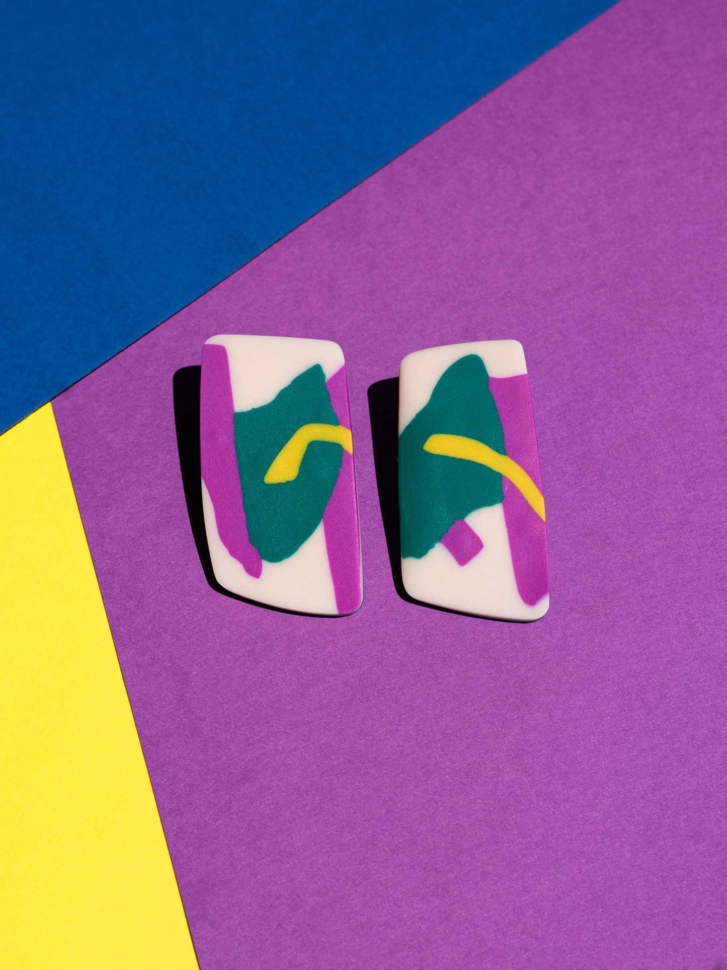 Front view of two original Salvaje studs, handmade in polymer clay, photographed on a colourful background under direct sunlight.