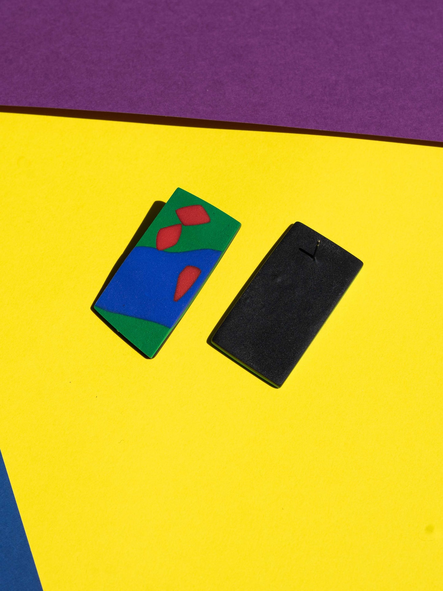 Front and back views of two original Salvaje studs, handmade in polymer clay, photographed on a colourful background under direct sunlight.