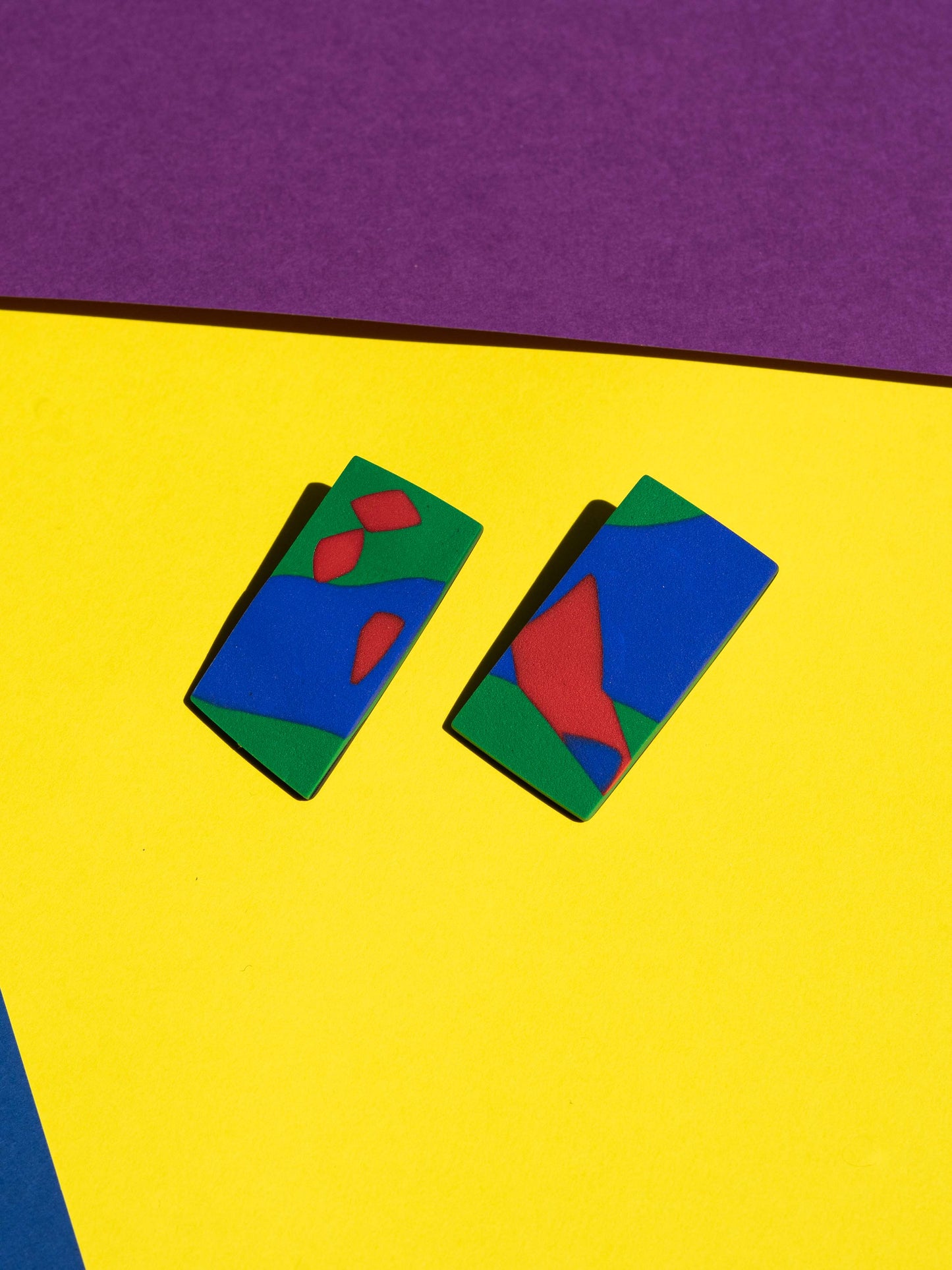 Front view of two original Salvaje studs, handmade in polymer clay, photographed on a colourful background under direct sunlight.