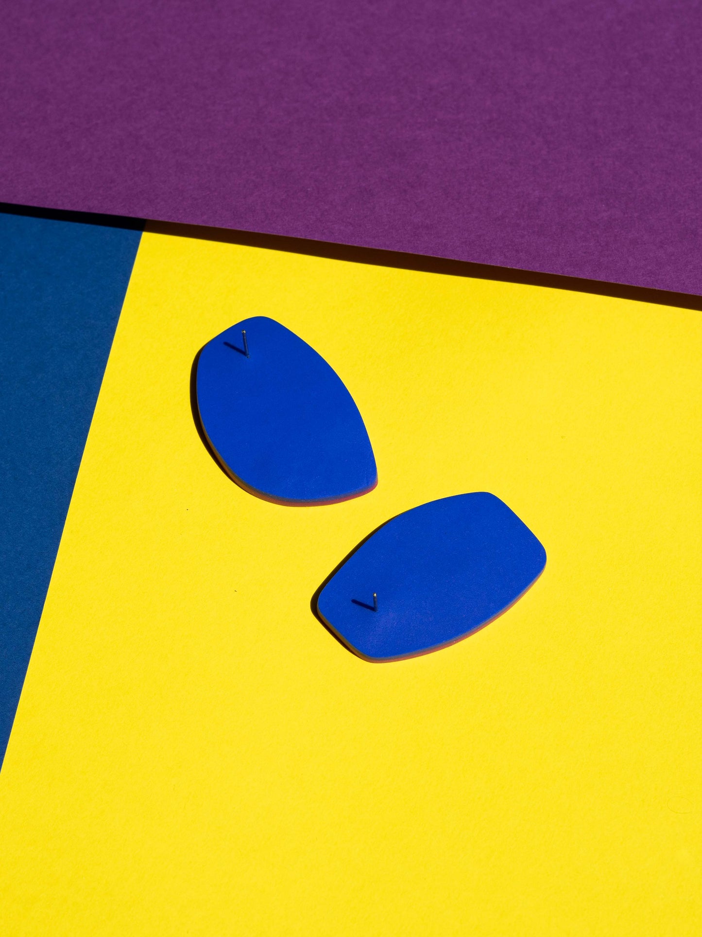 Back view of two original Salvaje studs, handmade in polymer clay, photographed on a colourful background under direct sunlight.