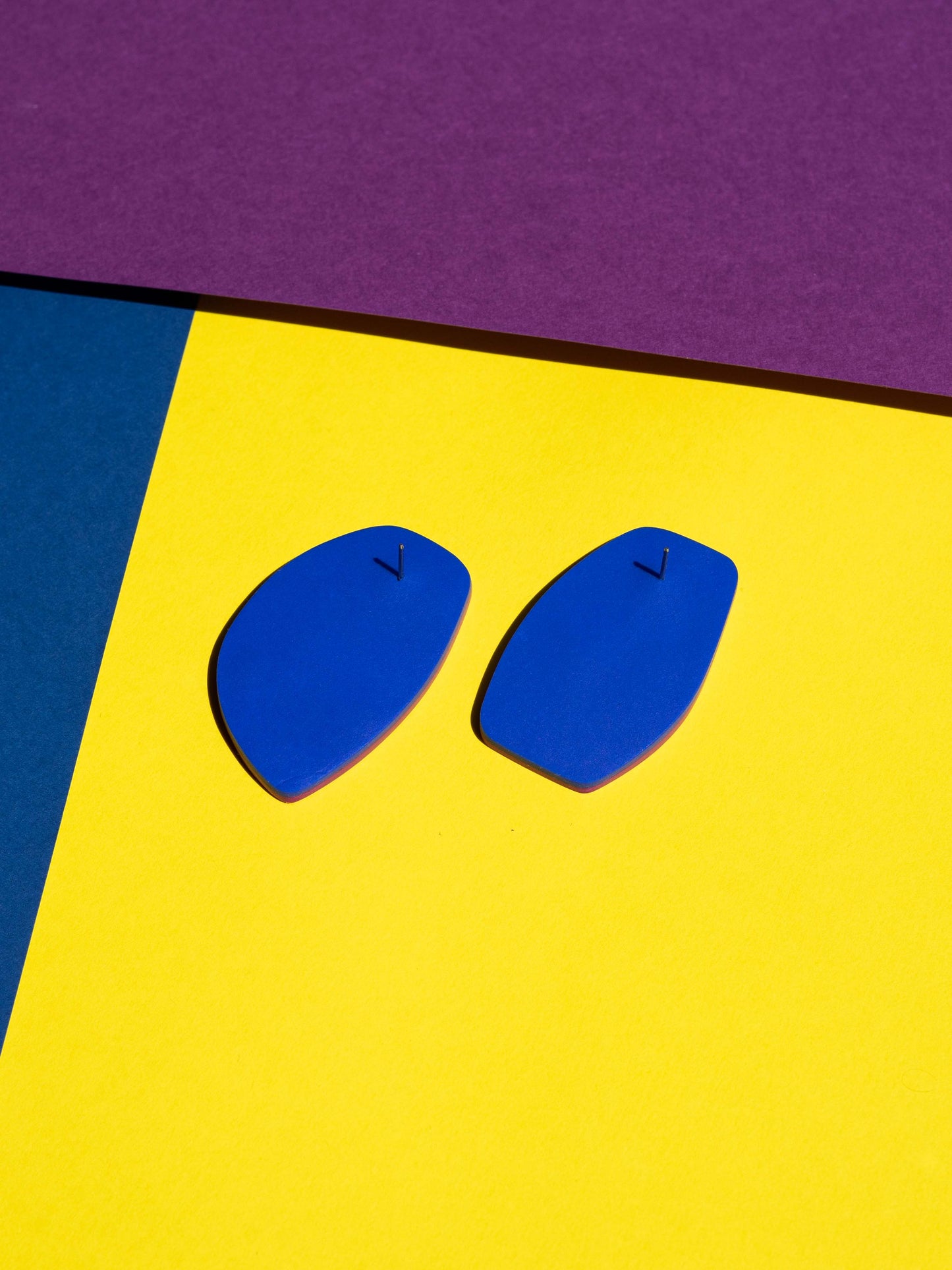 Back view of two original Salvaje studs, handmade in polymer clay, photographed on a colourful background under direct sunlight.