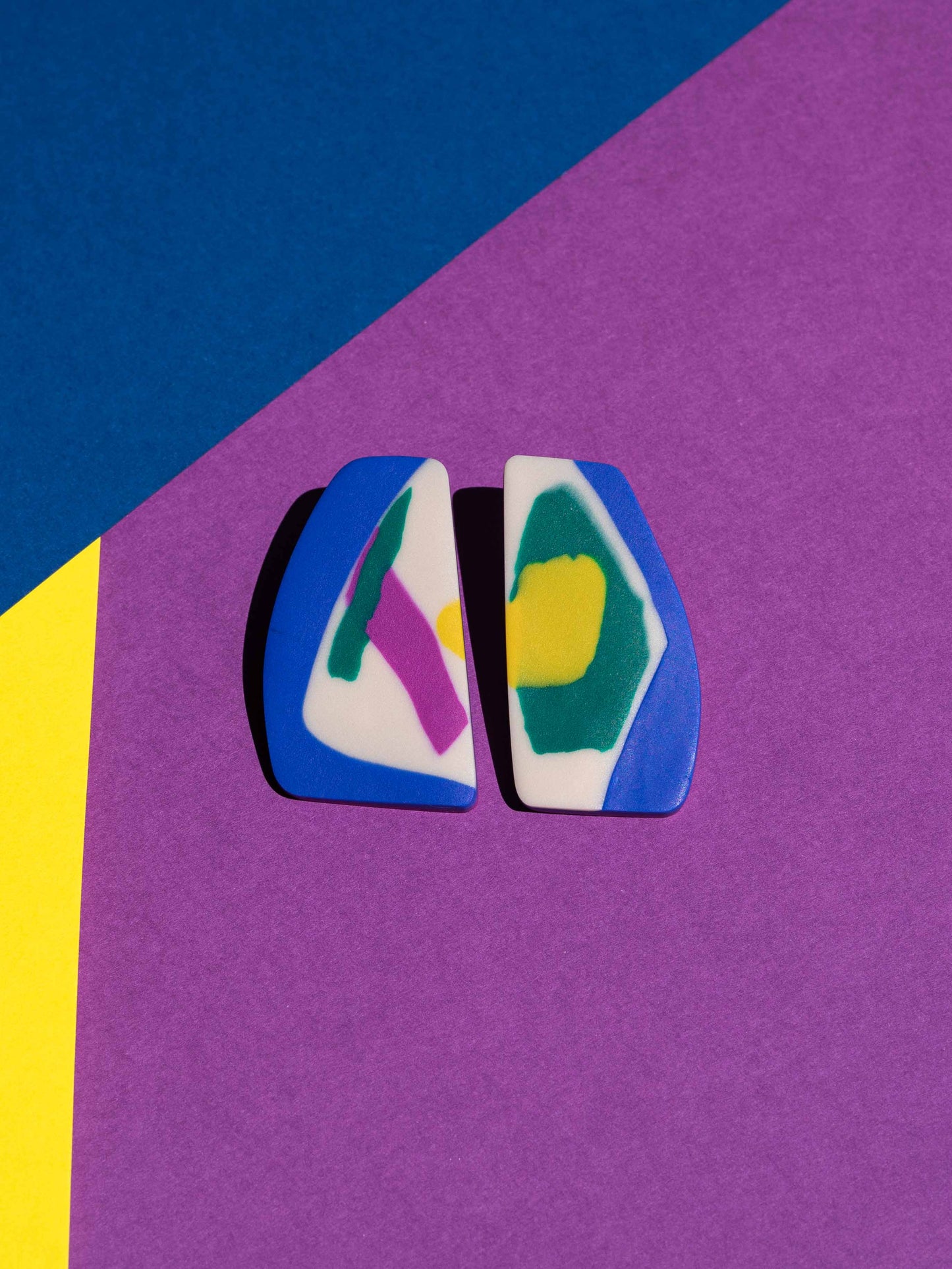 Front view of two original Salvaje studs, handmade in polymer clay, photographed on a colourful background under direct sunlight.