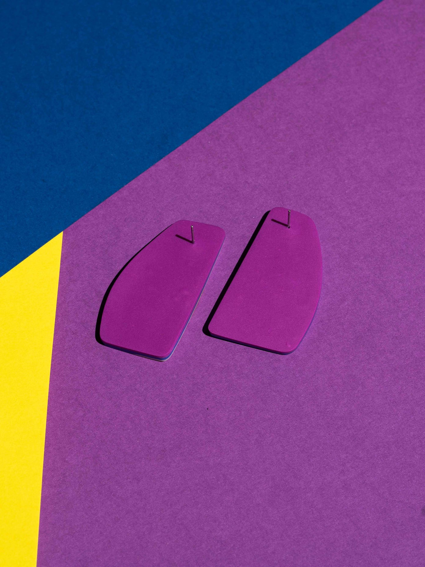 Back view of two original Salvaje studs, handmade in polymer clay, photographed on a colourful background under direct sunlight.