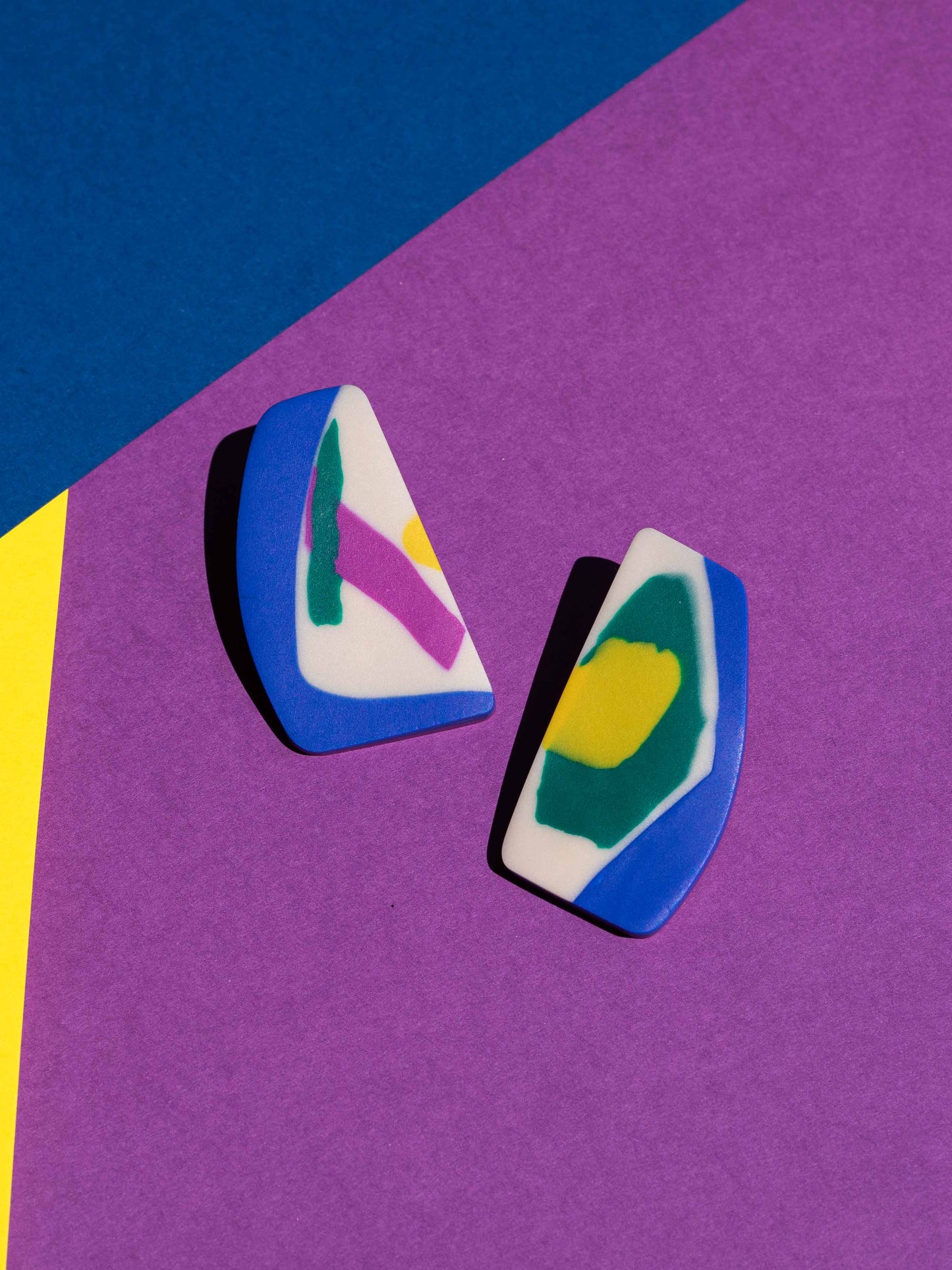 Front view of two original Salvaje studs, handmade in polymer clay, photographed on a colourful background under direct sunlight.