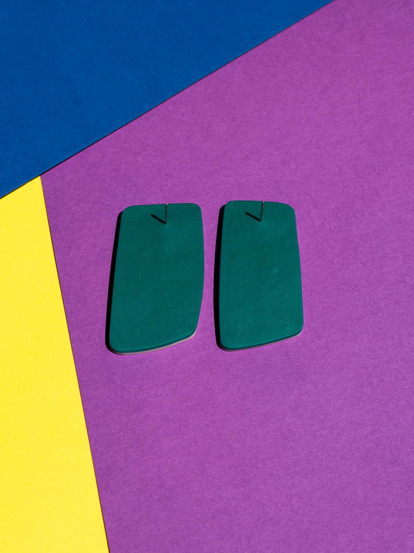 Back view of two original Salvaje studs, handmade in polymer clay, photographed on a colourful background under direct sunlight.
