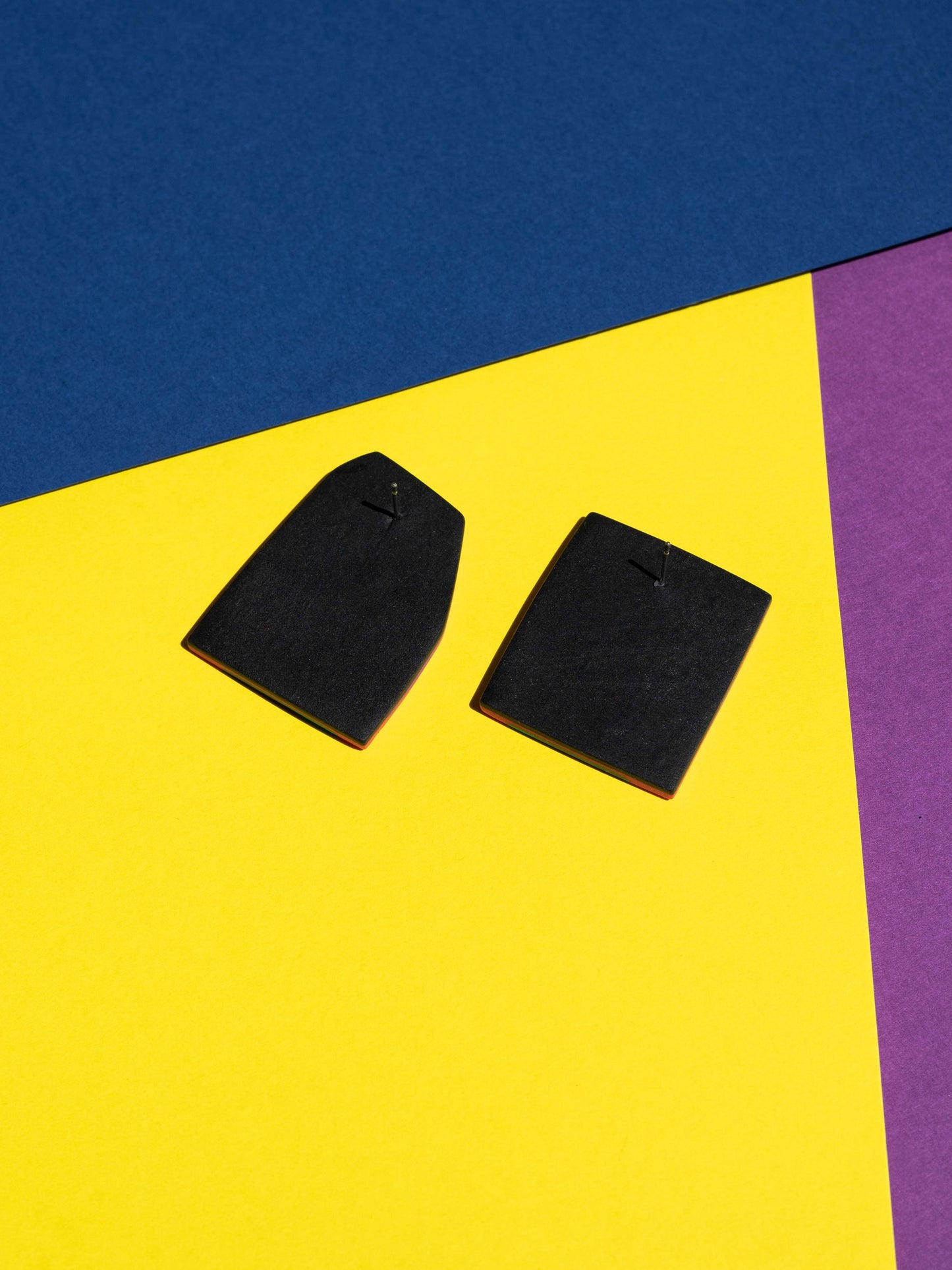 Back view of two original Salvaje studs, handmade in polymer clay, photographed on a colourful background under direct sunlight.