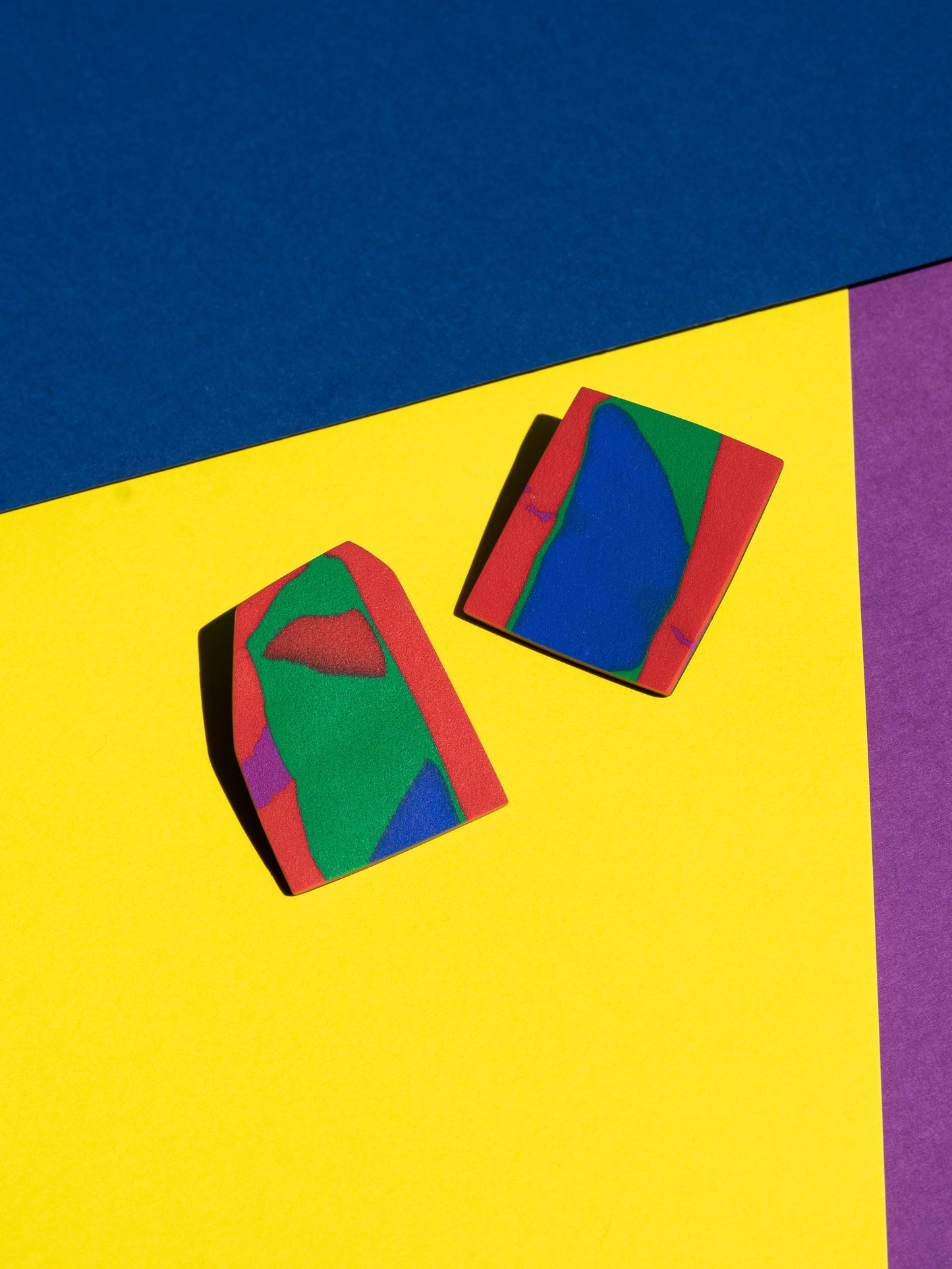 Front view of two original Salvaje studs, handmade in polymer clay, photographed on a colourful background under direct sunlight.