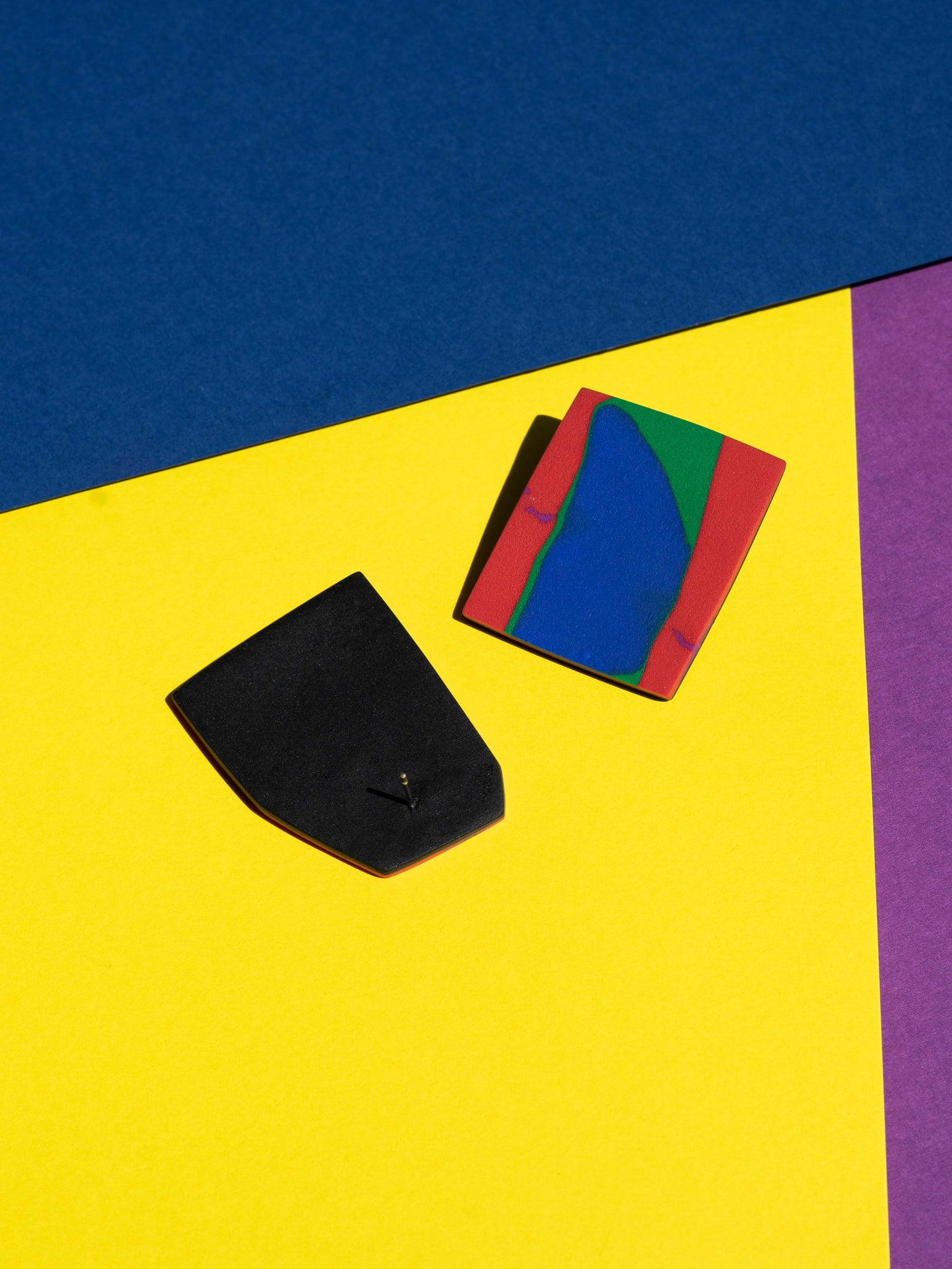 Front and back views of two original Salvaje studs, handmade in polymer clay, photographed on a colourful background under direct sunlight.