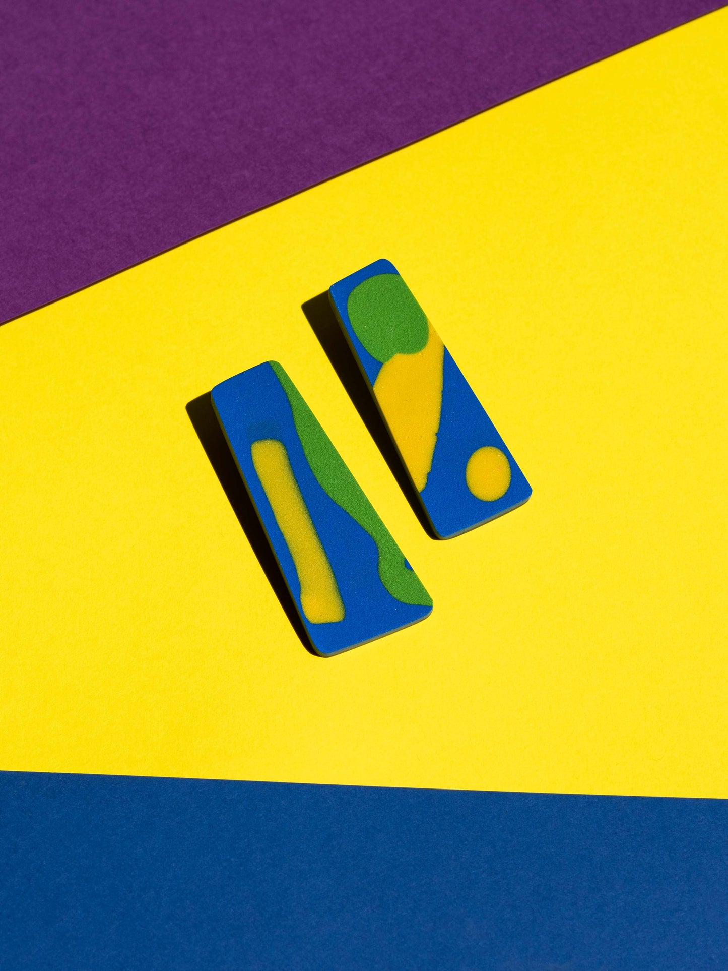 Front view of two original Salvaje studs, handmade in polymer clay, photographed on a colourful background under direct sunlight.