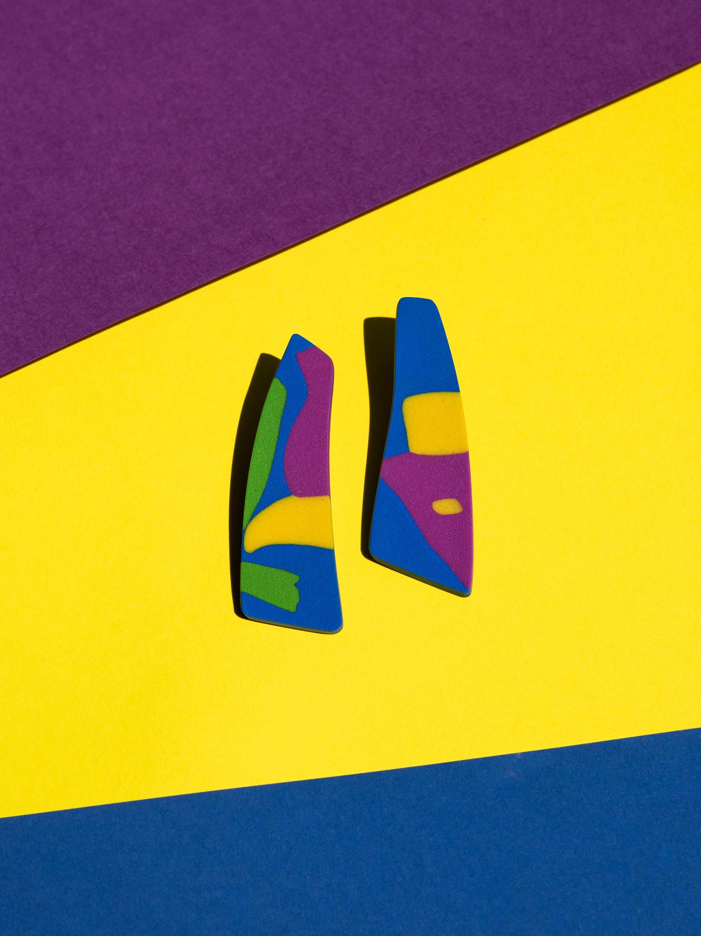Front view of two original Salvaje studs, handmade in polymer clay, photographed on a colourful background under direct sunlight.