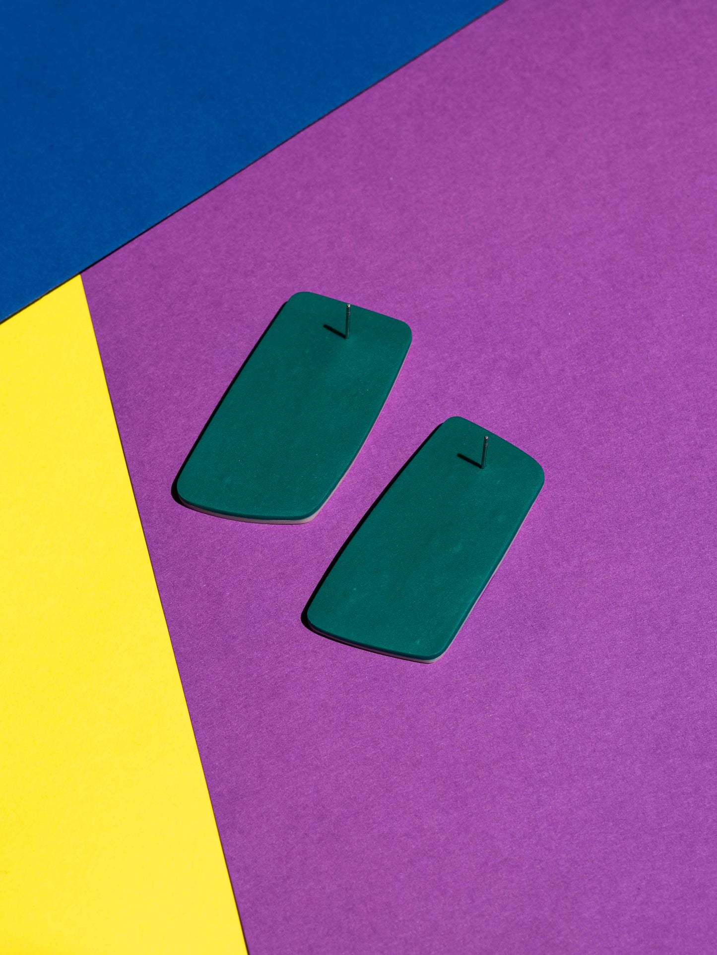 Back view of two original Salvaje studs, handmade in polymer clay, photographed on a colourful background under direct sunlight.