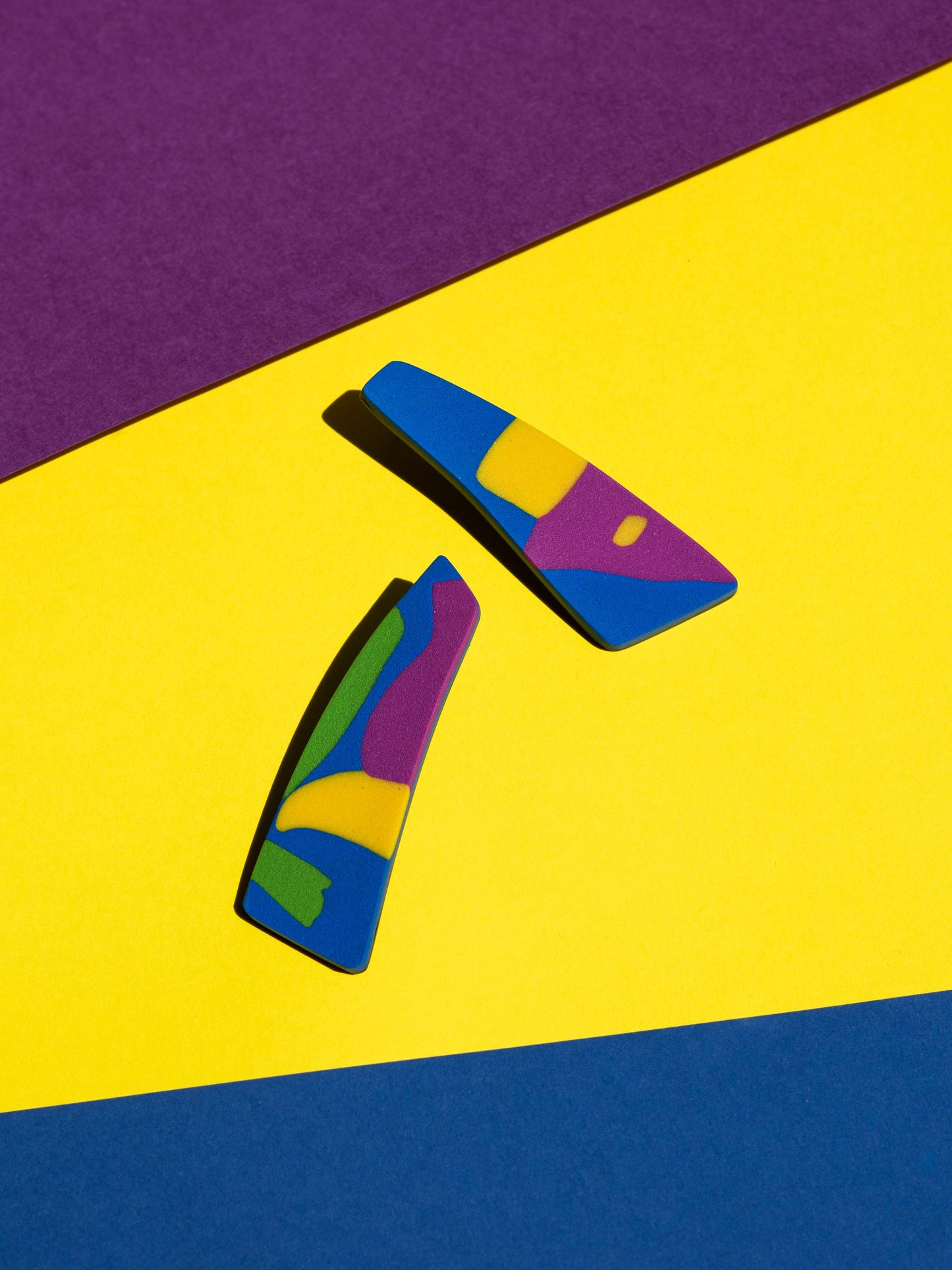Front view of two original Salvaje studs, handmade in polymer clay, photographed on a colourful background under direct sunlight.