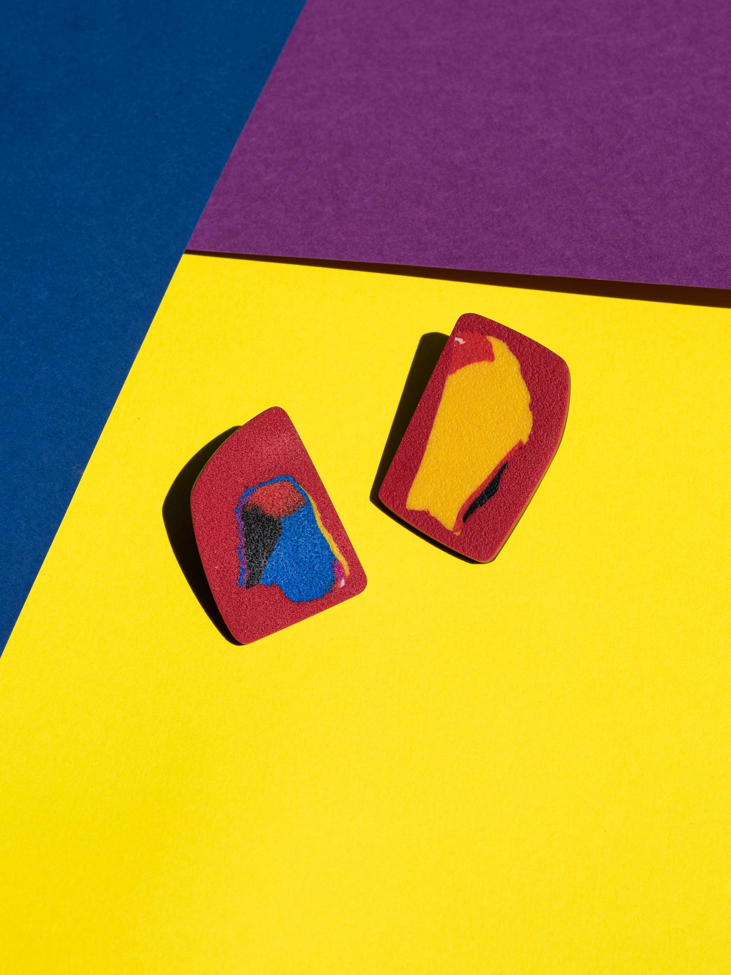 Front view of two original Salvaje studs, handmade in polymer clay, photographed on a colourful background under direct sunlight.