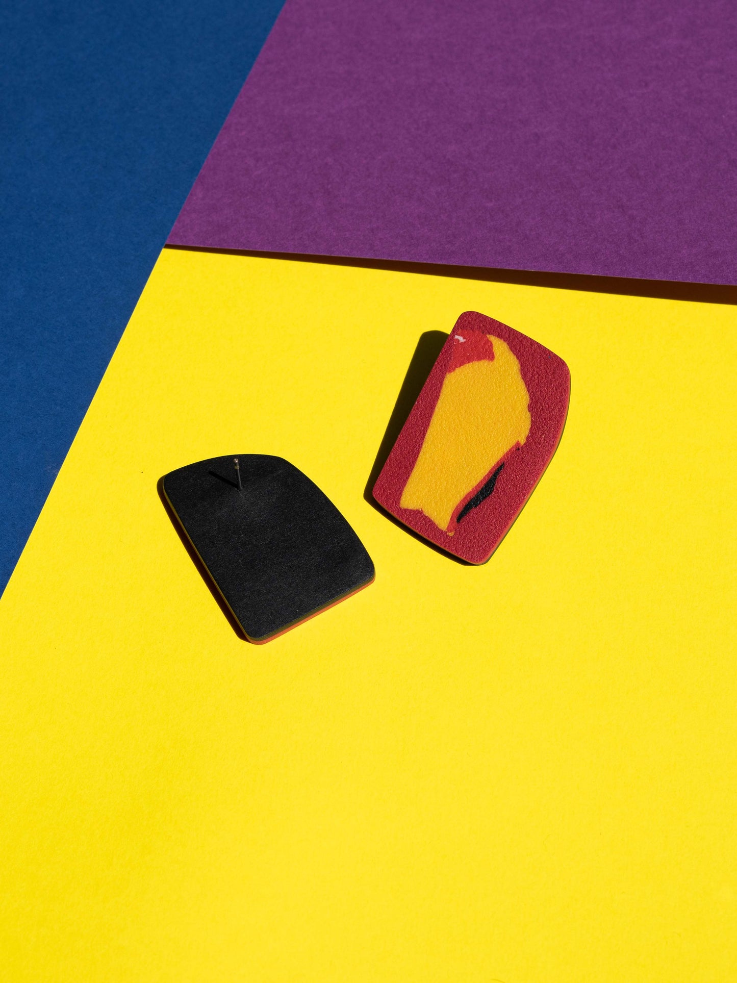 Back and front views of two original Salvaje studs, handmade in polymer clay, photographed on a colourful background under direct sunlight.