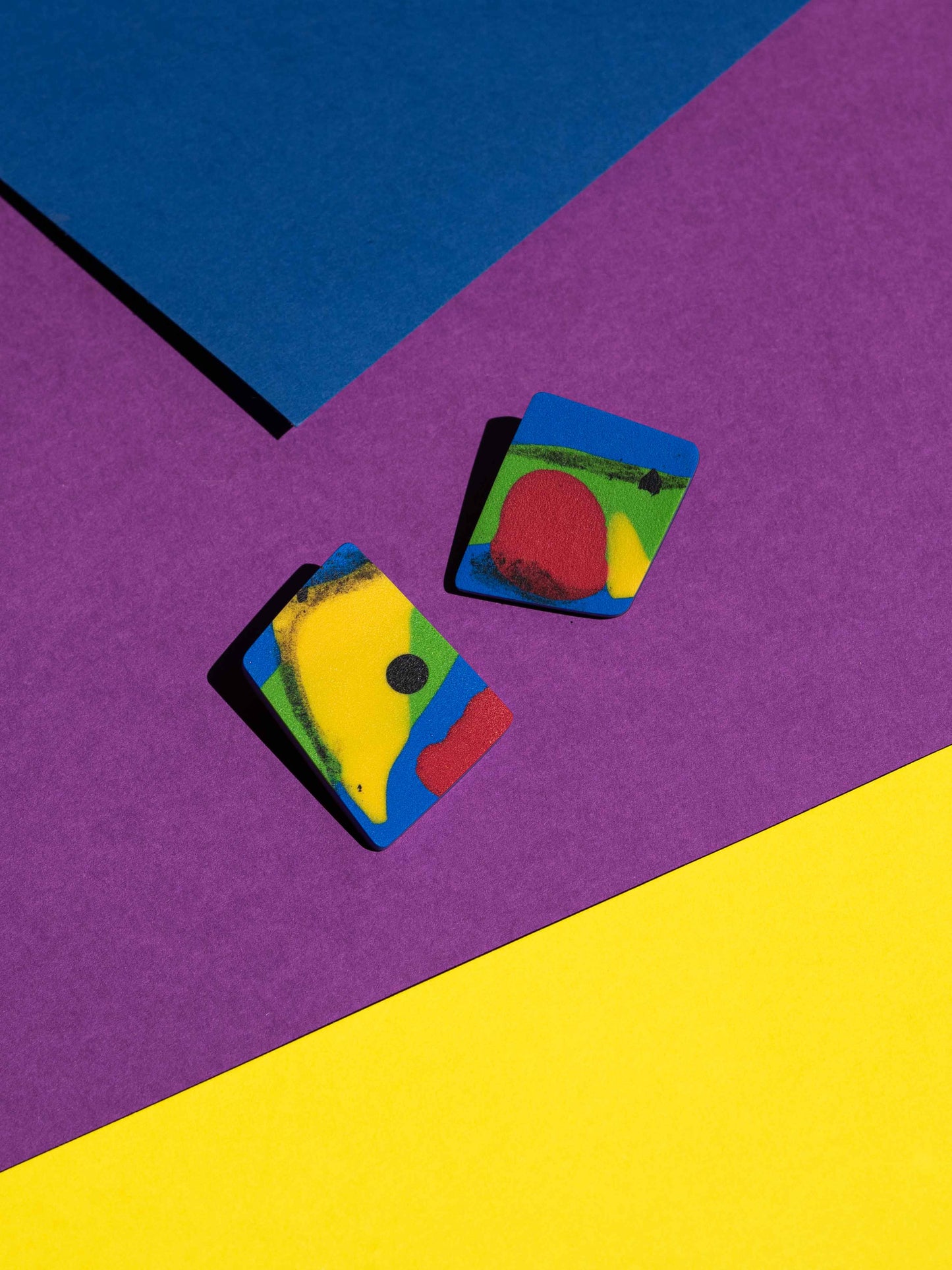 Front view of two original Salvaje studs, handmade in polymer clay, photographed on a colourful background under direct sunlight.