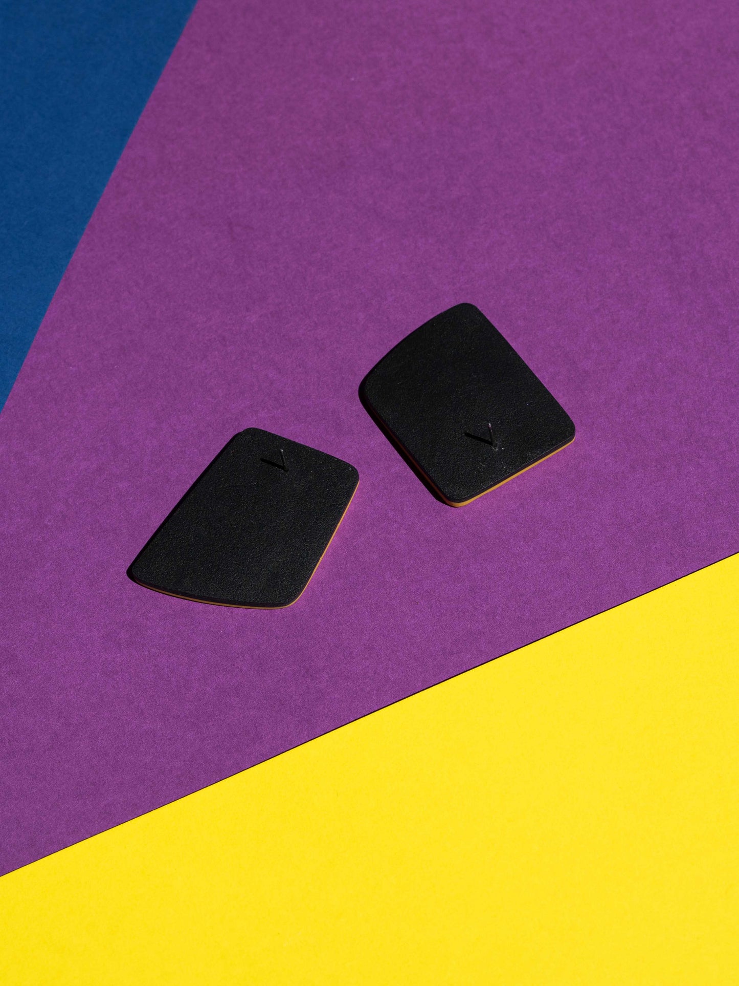 Back view of two original Salvaje studs, handmade in polymer clay, photographed on a colourful background under direct sunlight.