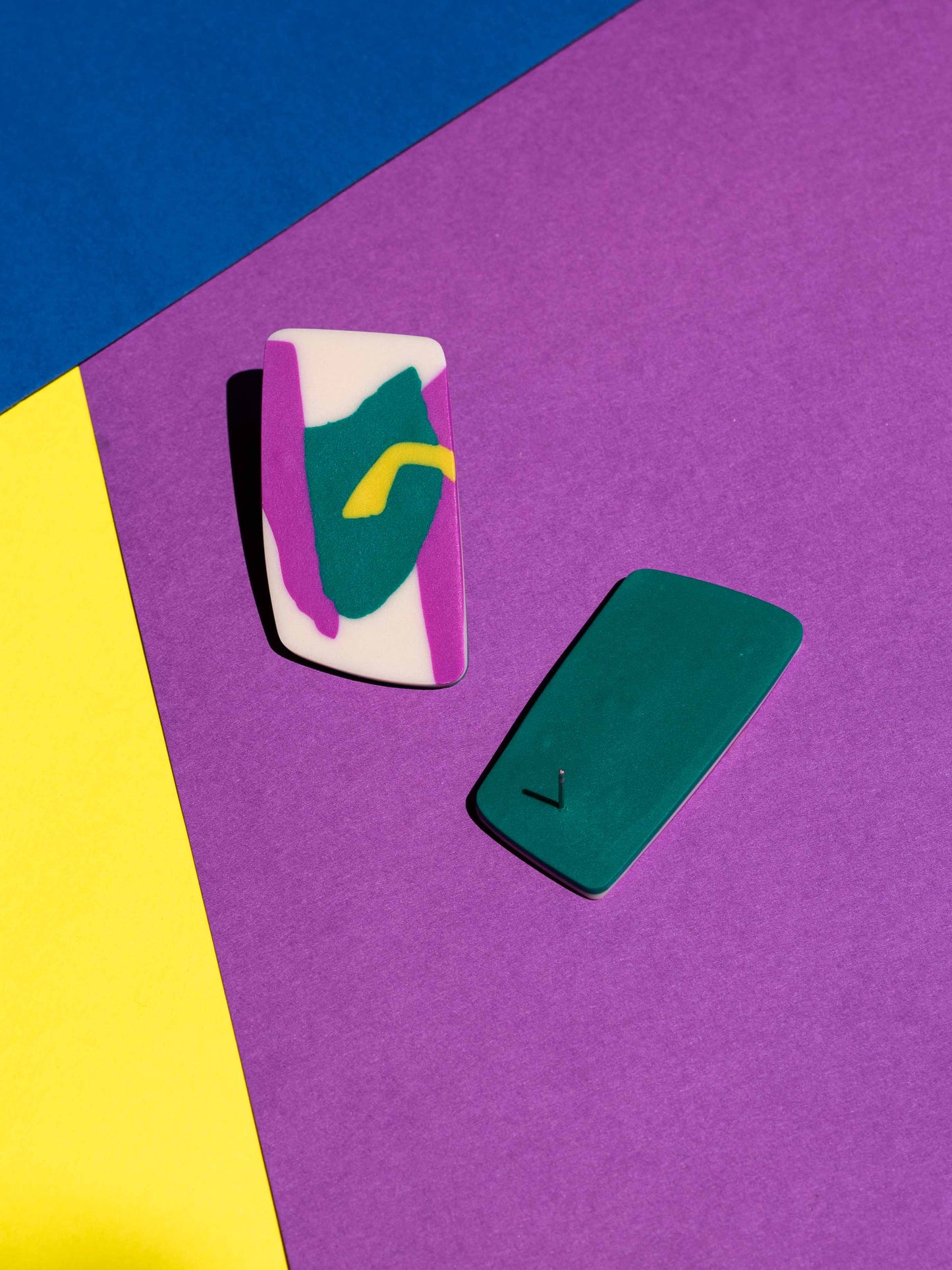 Front and back views of two original Salvaje studs, handmade in polymer clay, photographed on a colourful background under direct sunlight.