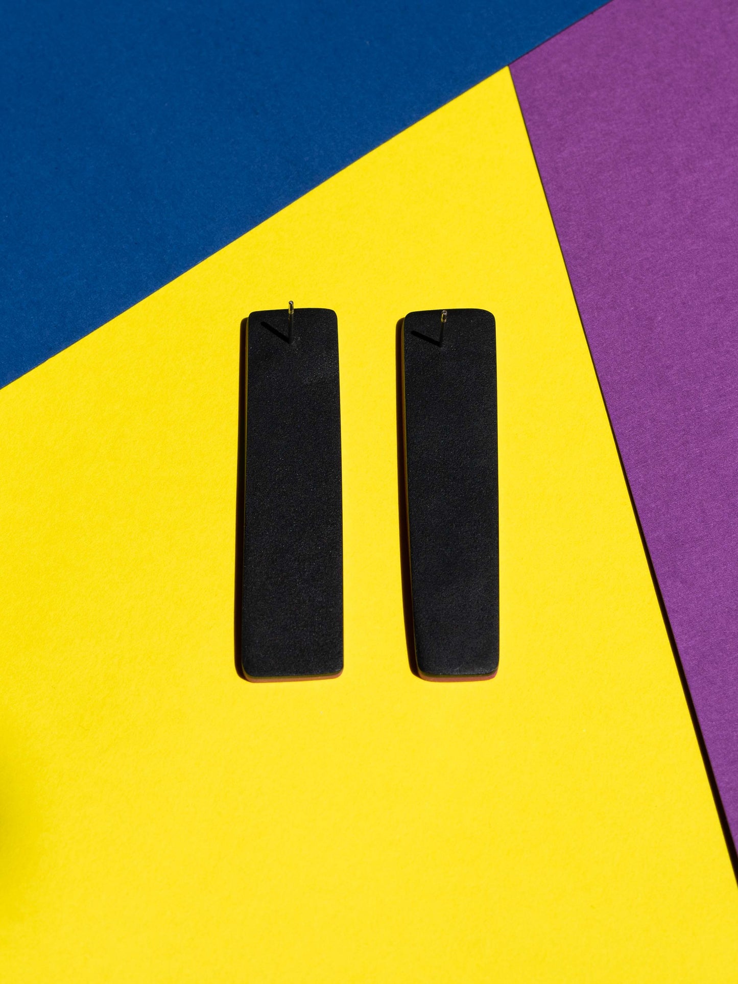 Back view of two original Salvaje studs, handmade in polymer clay, photographed on a colourful background under direct sunlight.