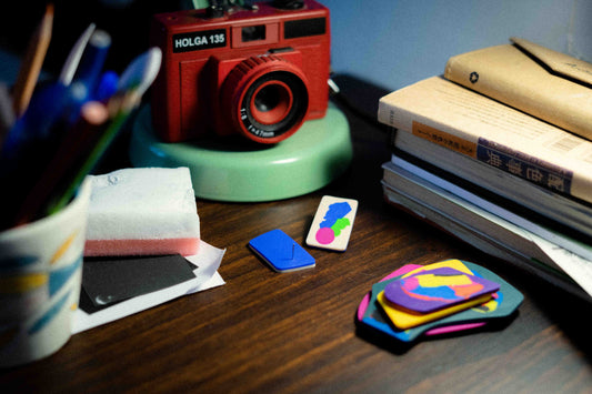 Studs placed on a desk surrounded by books, an analogue camera, a cup with colours, and other personal objects