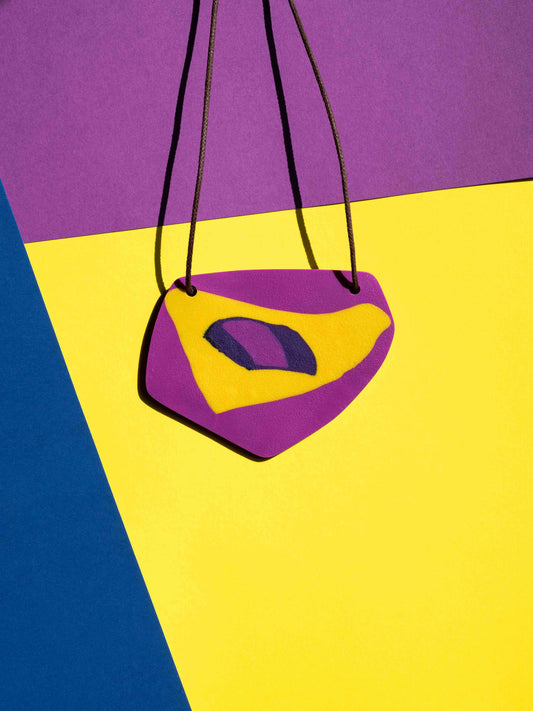 Front view of a salvaje pendant in magenta, yellow and purple colours with strong lighting on a colourful background