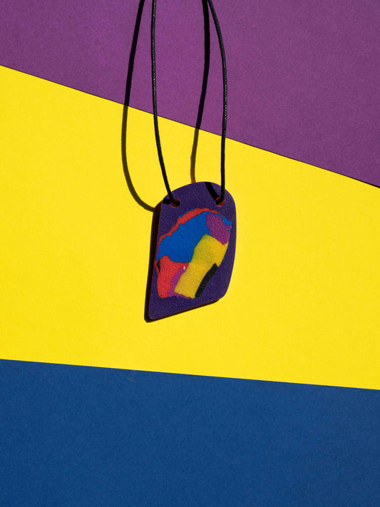 Front view of a salvaje pendant in purple, magenta, yellow, blue, black and red colours with strong lighting on a colourful background