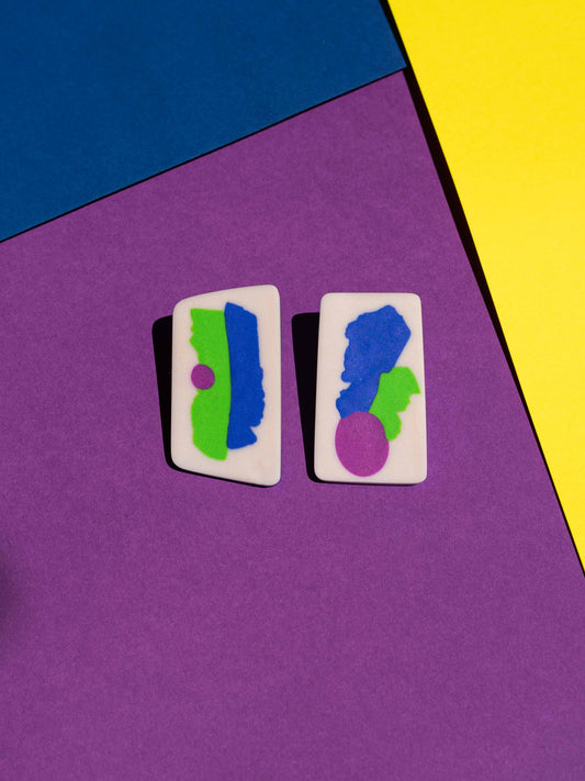 Front view of two original Salvaje studs, handmade in polymer clay, photographed on a colourful background under direct sunlight.