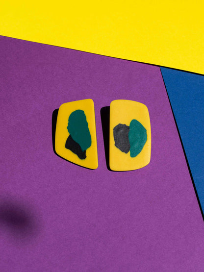 Front view of two original Salvaje studs, handmade in polymer clay, photographed on a colourful background under direct sunlight.