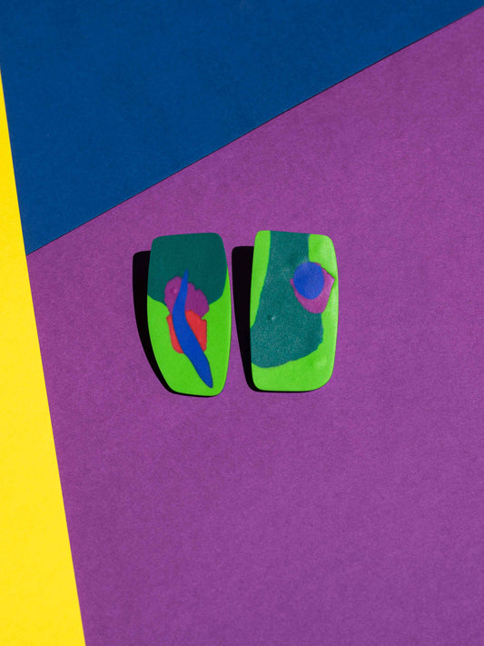 Front view of two original Salvaje studs, handmade in polymer clay, photographed on a colourful background under direct sunlight.