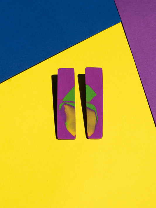 Front view of two original Salvaje studs, handmade in polymer clay, photographed on a colourful background under direct sunlight.