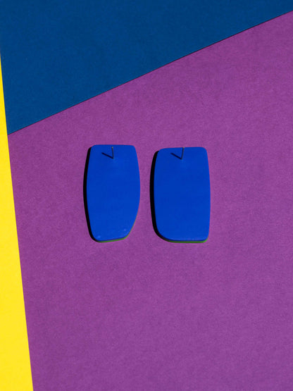 Back view of two original Salvaje studs, handmade in polymer clay, photographed on a colourful background under direct sunlight.