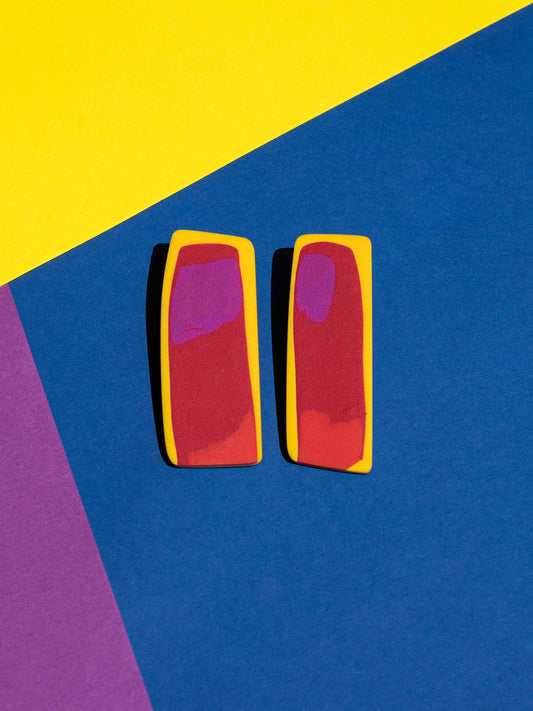 Front view of two original Salvaje studs, handmade in polymer clay, photographed on a colourful background under direct sunlight.