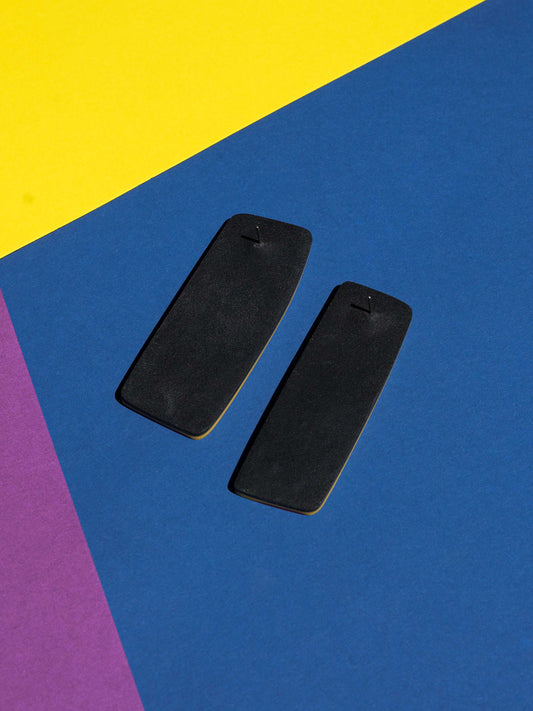 Back view of two original Salvaje studs, handmade in polymer clay, photographed on a colourful background under direct sunlight.