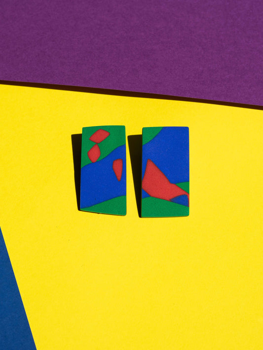 Front view of two original Salvaje studs, handmade in polymer clay, photographed on a colourful background under direct sunlight.