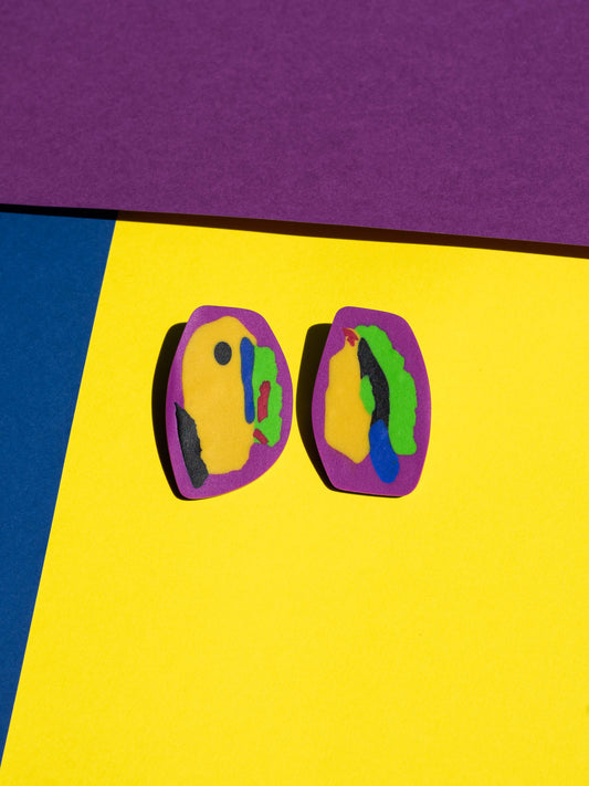 Front view of two original Salvaje studs, handmade in polymer clay, photographed on a colourful background under direct sunlight.