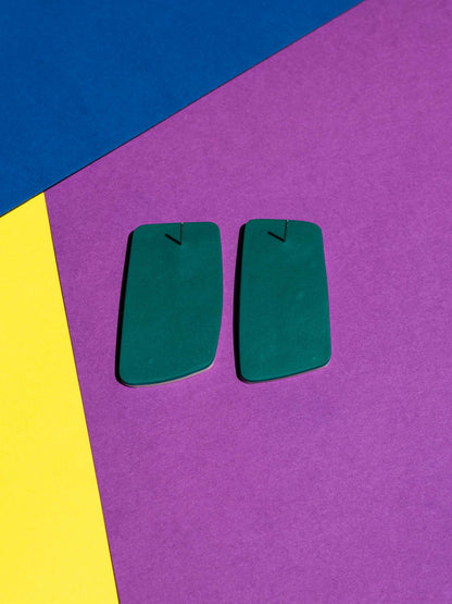 Back view of two original Salvaje studs, handmade in polymer clay, photographed on a colourful background under direct sunlight.