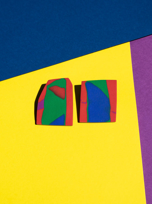 Front view of two original Salvaje studs, handmade in polymer clay, photographed on a colourful background under direct sunlight.